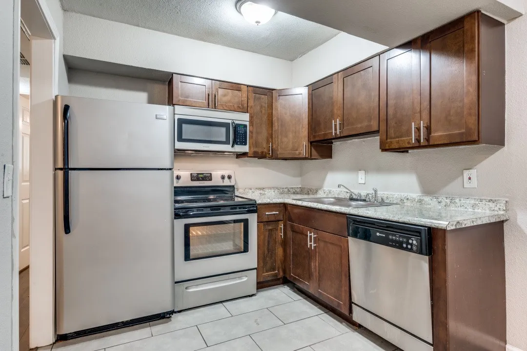 Kitchen featuring wood-finish cabinetry, stainless steel appliances, speckled countertops, and tile flooring