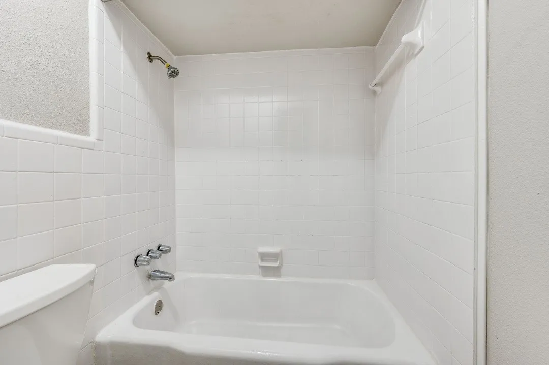 White tiled bath and shower combination with a fixed showerhead and chrome fixtures