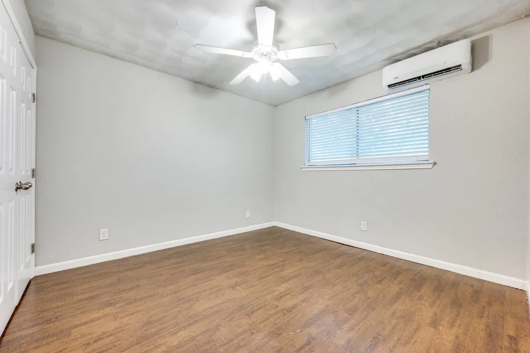 Wood-finish flooring, white ceiling fan, horizontal window blinds, and a wall-mounted mini-split system