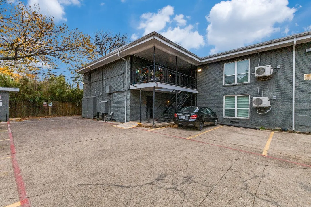 Paved parking area, gray brick exterior, white-framed windows, exterior staircase, upper-level balcony