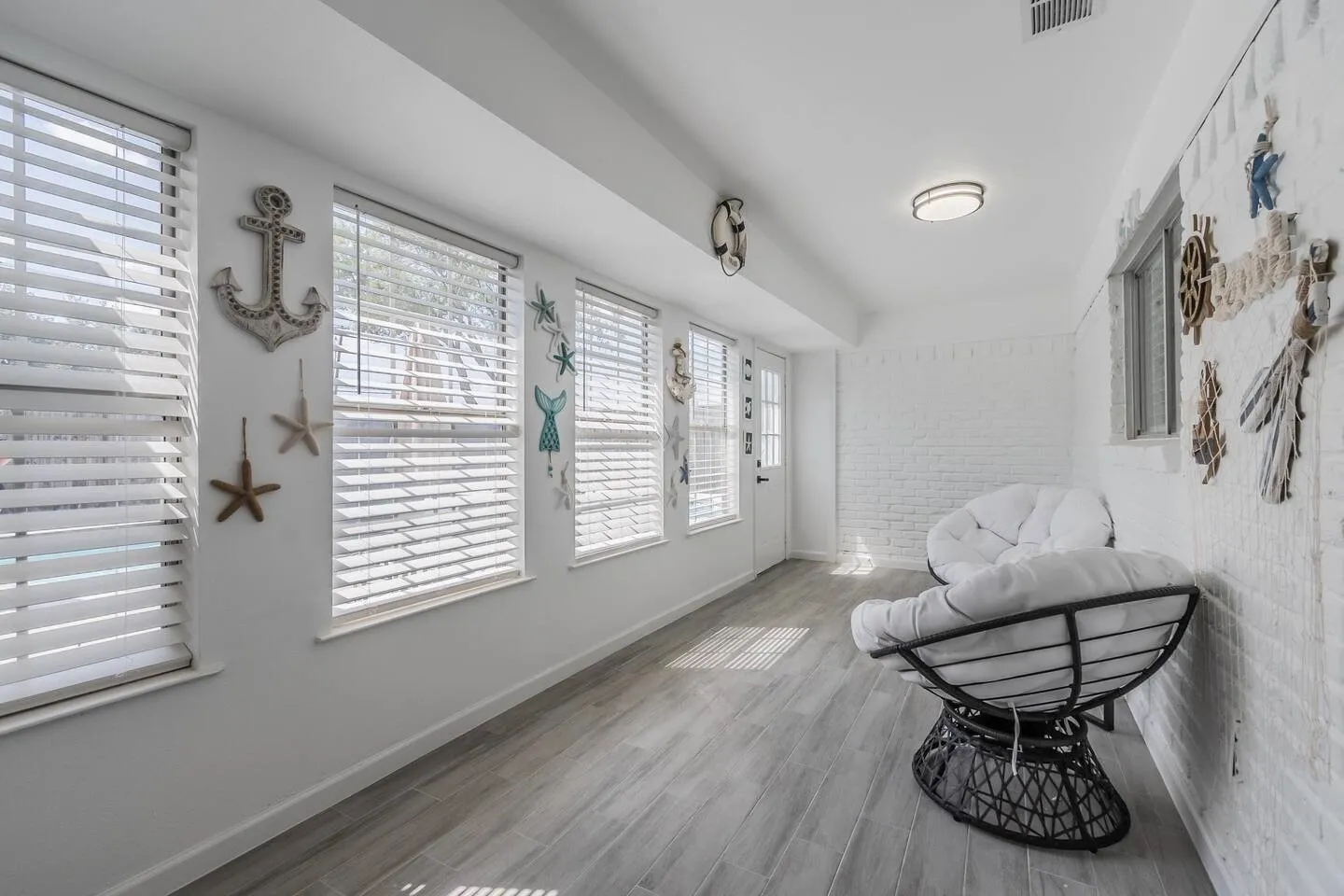 White painted brick wall, recessed lighting, wood-finish flooring, multiple windows with blinds, and a white door with frosted glass panes