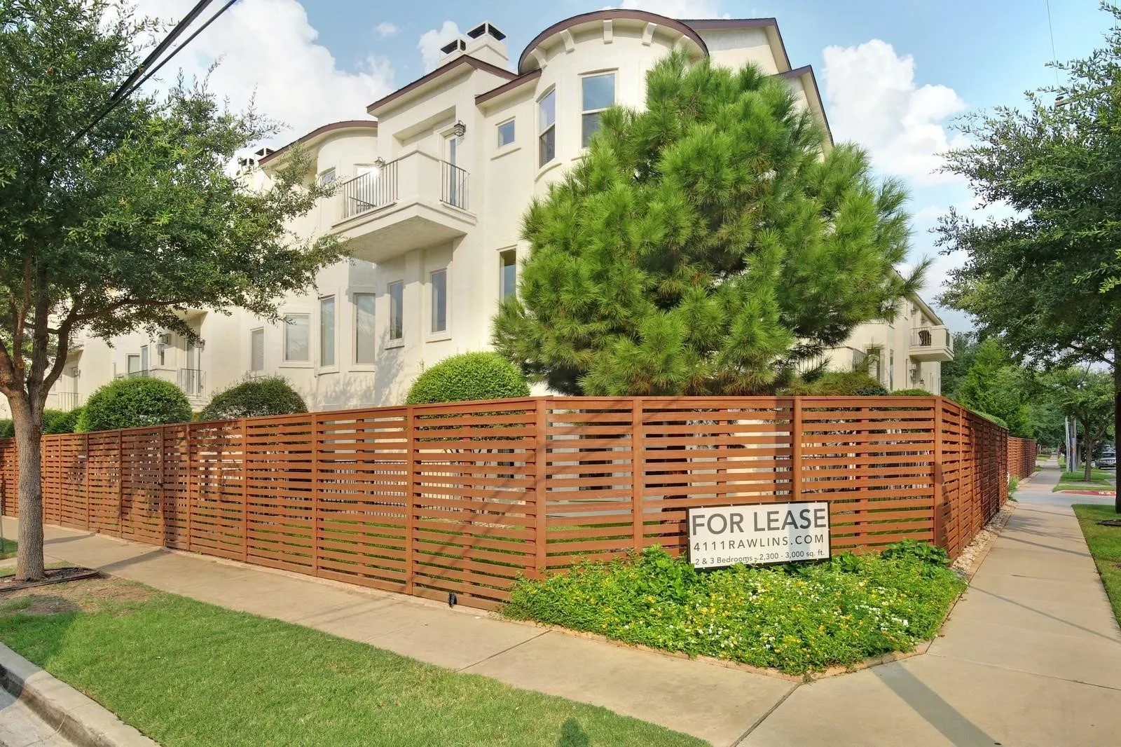 Light-colored stucco exterior with multiple balconies, featuring a contemporary slatted wood fence