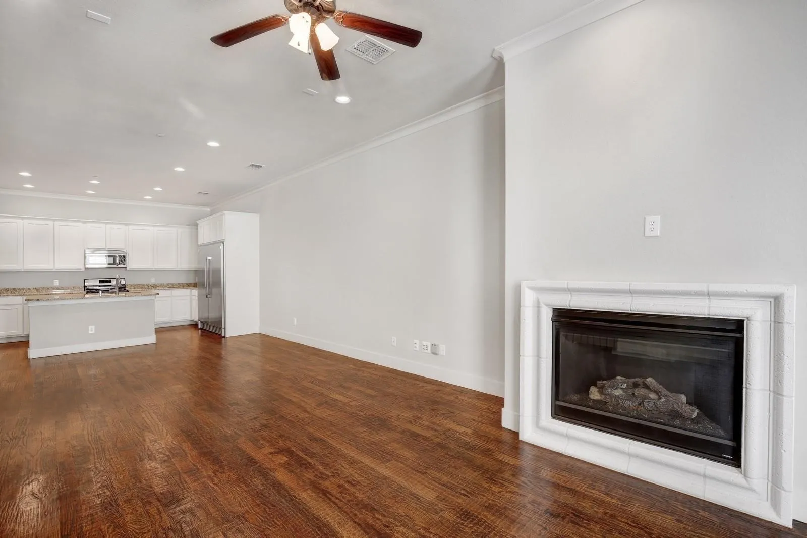 Living area featuring wood-finish flooring, a ceiling fan, crown molding, and a tiled fireplace