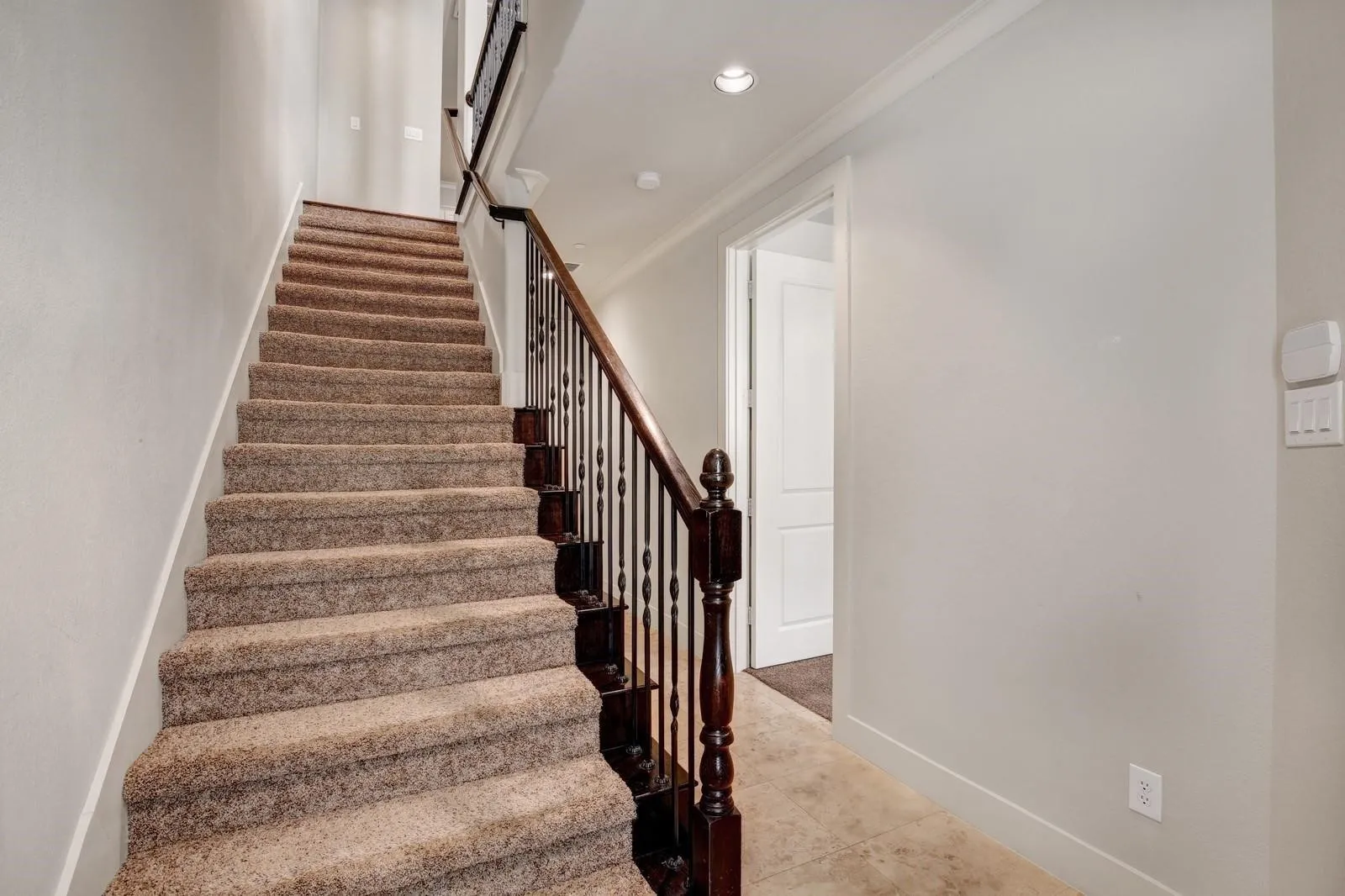 Carpeted staircase with dark wood newel post and wrought iron balusters