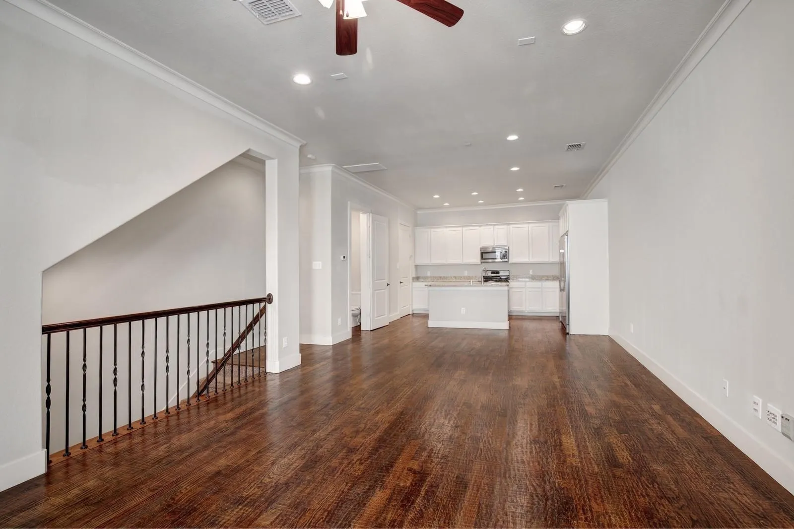 Wood-finish flooring, white walls, recessed lighting, and a white kitchen with stainless steel appliances