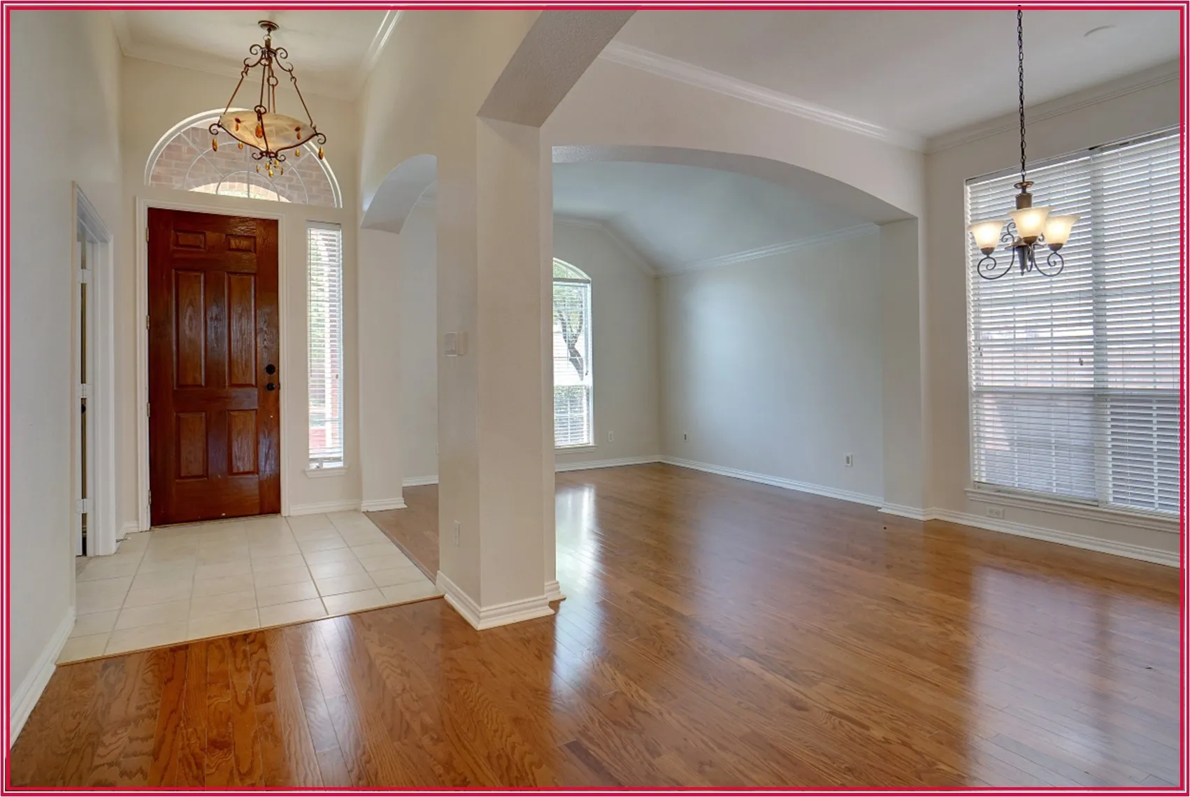 Hardwood flooring throughout, arched doorways, tile entry, transom window, and a decorative chandelier
