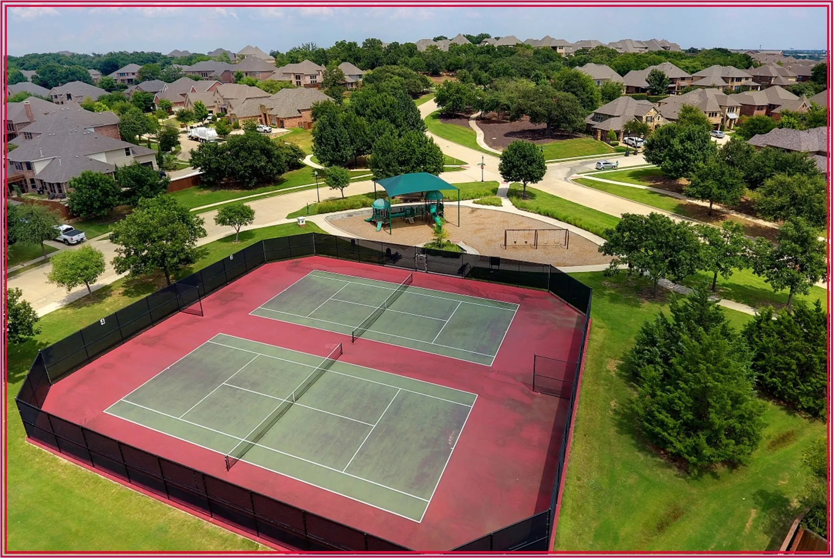 Dual tennis courts with perimeter fencing, surrounded by a landscaped common area featuring a playground structure and open green spaces