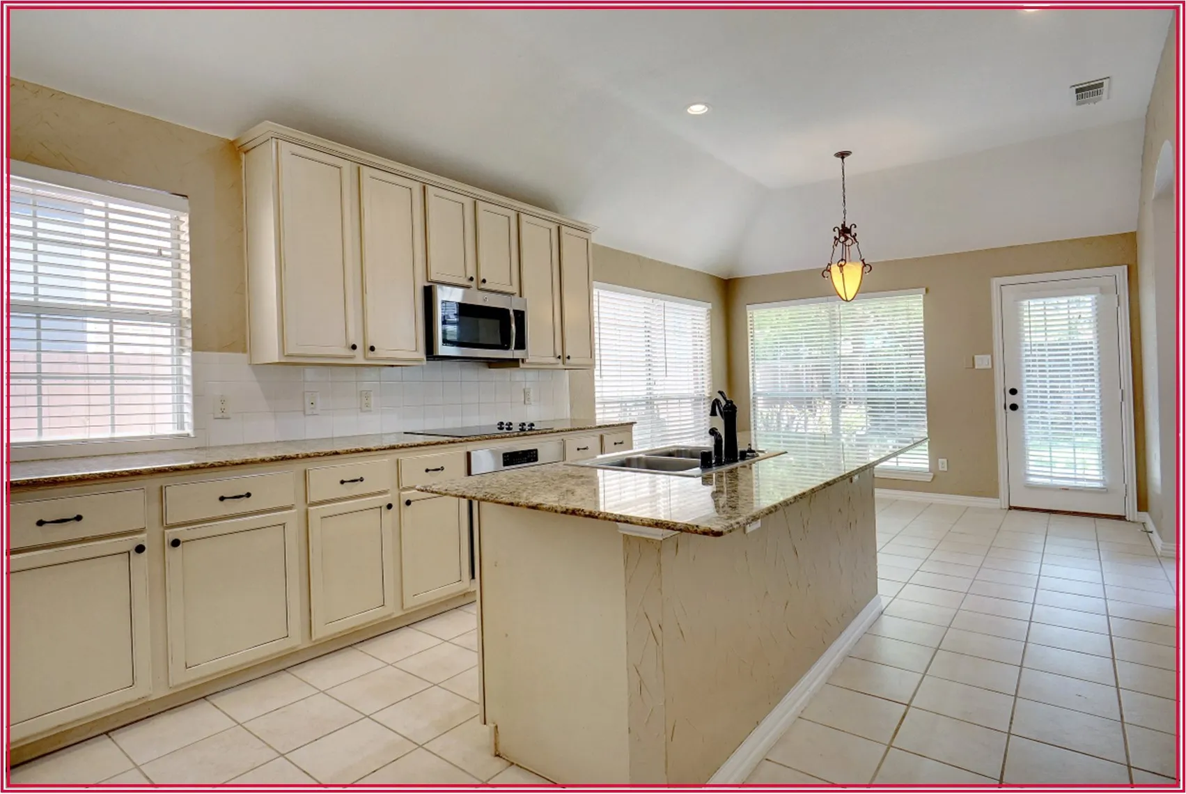 Kitchen featuring an island with a dual-basin sink, white cabinetry with dark hardware, granite-style countertops, and a white tile backsplash