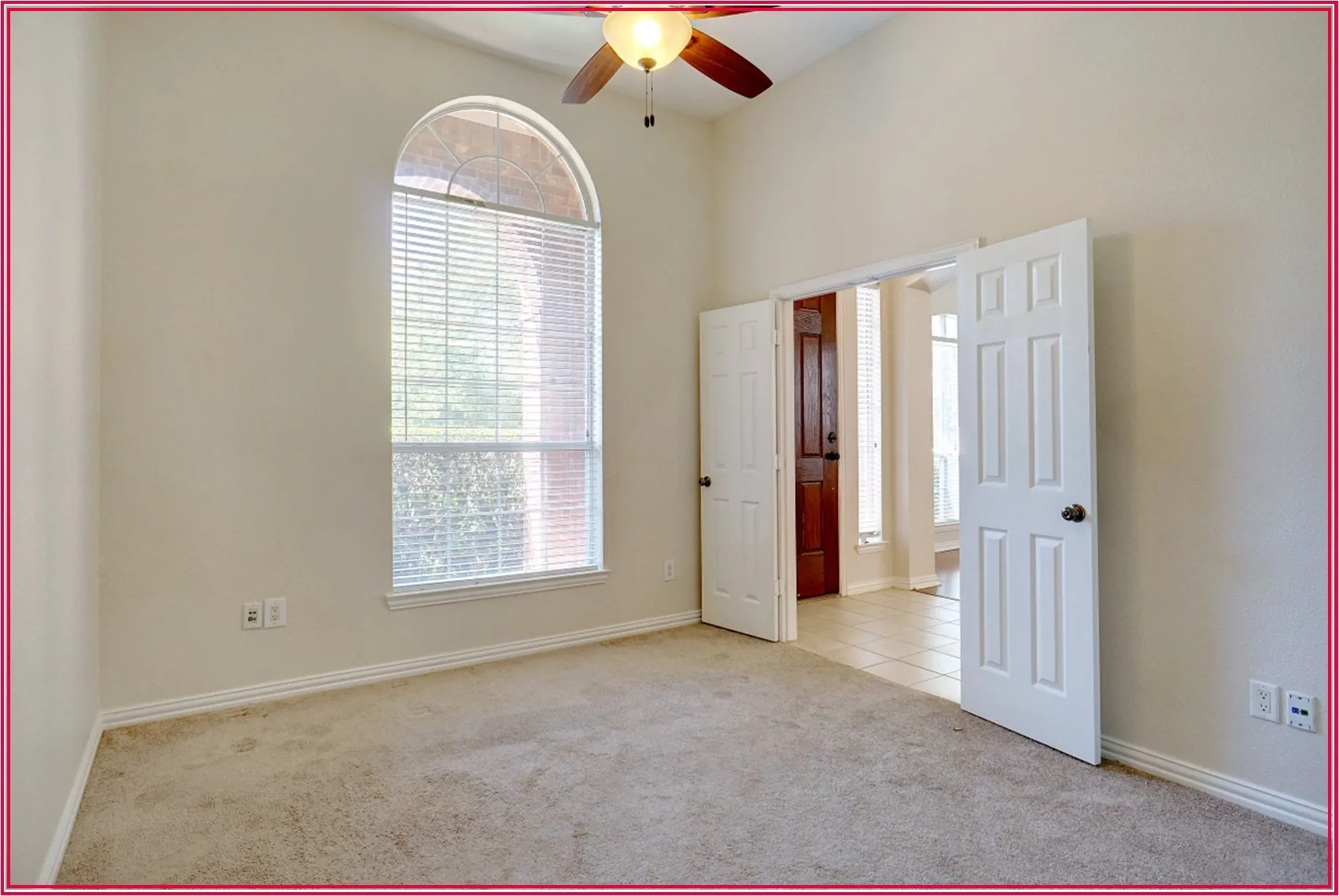 Arched window with blinds, carpeted flooring, ceiling fan, and double panel doors