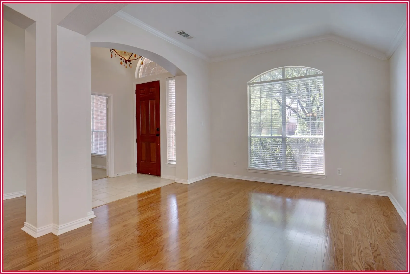 Wood-finish flooring, arched entryway, vaulted ceiling, arched window, and a paneled front door