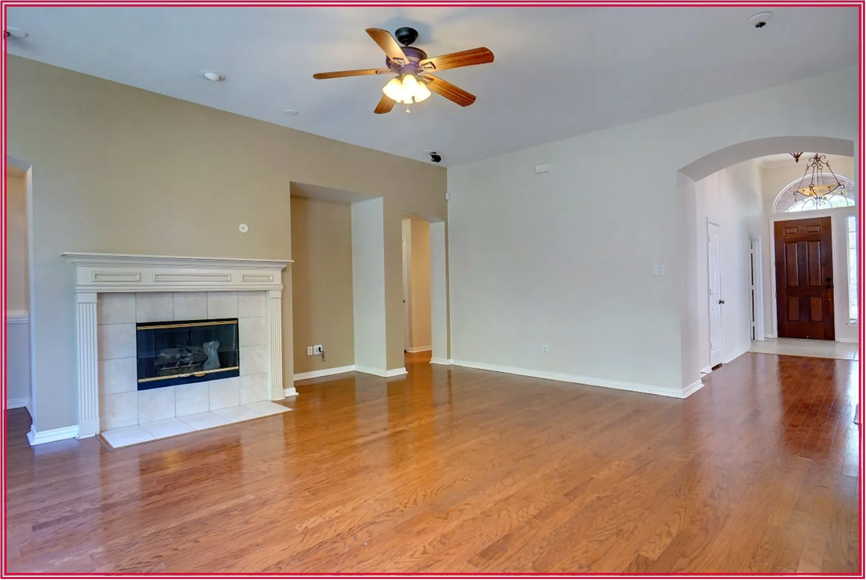 Vaulted ceiling with a ceiling fan, hardwood-finish flooring, fireplace with a tile surround and mantel, arched entryway, and a solid wood front door