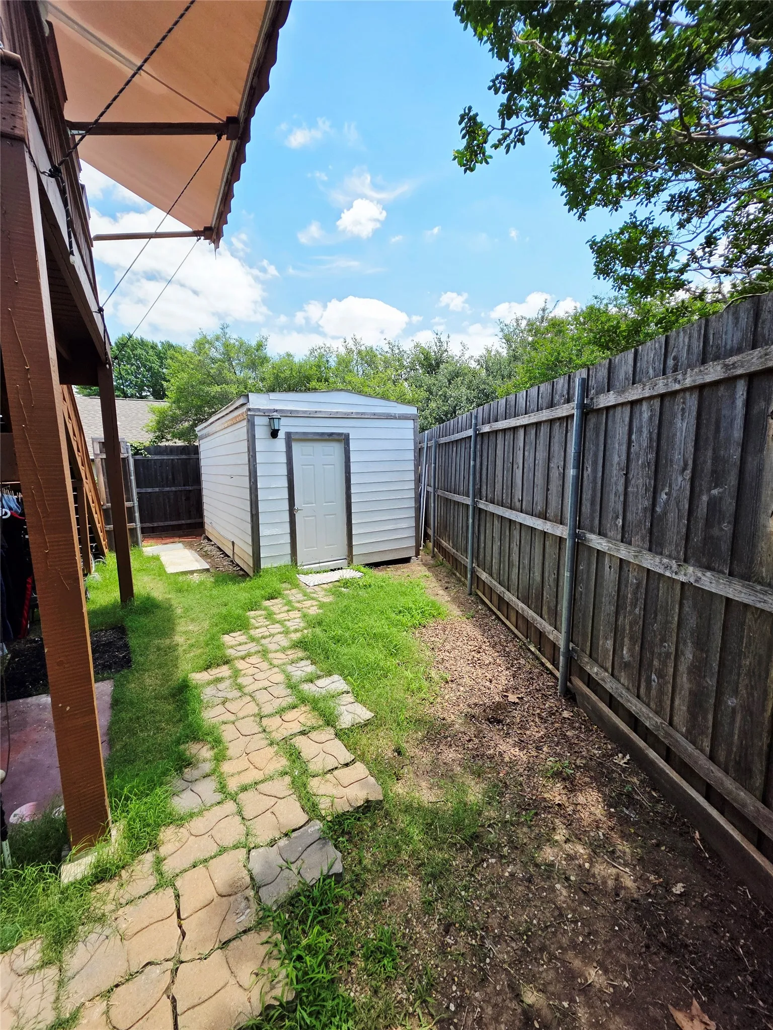 Wood privacy fencing with a storage shed, featuring a covered patio area and stone paver pathway