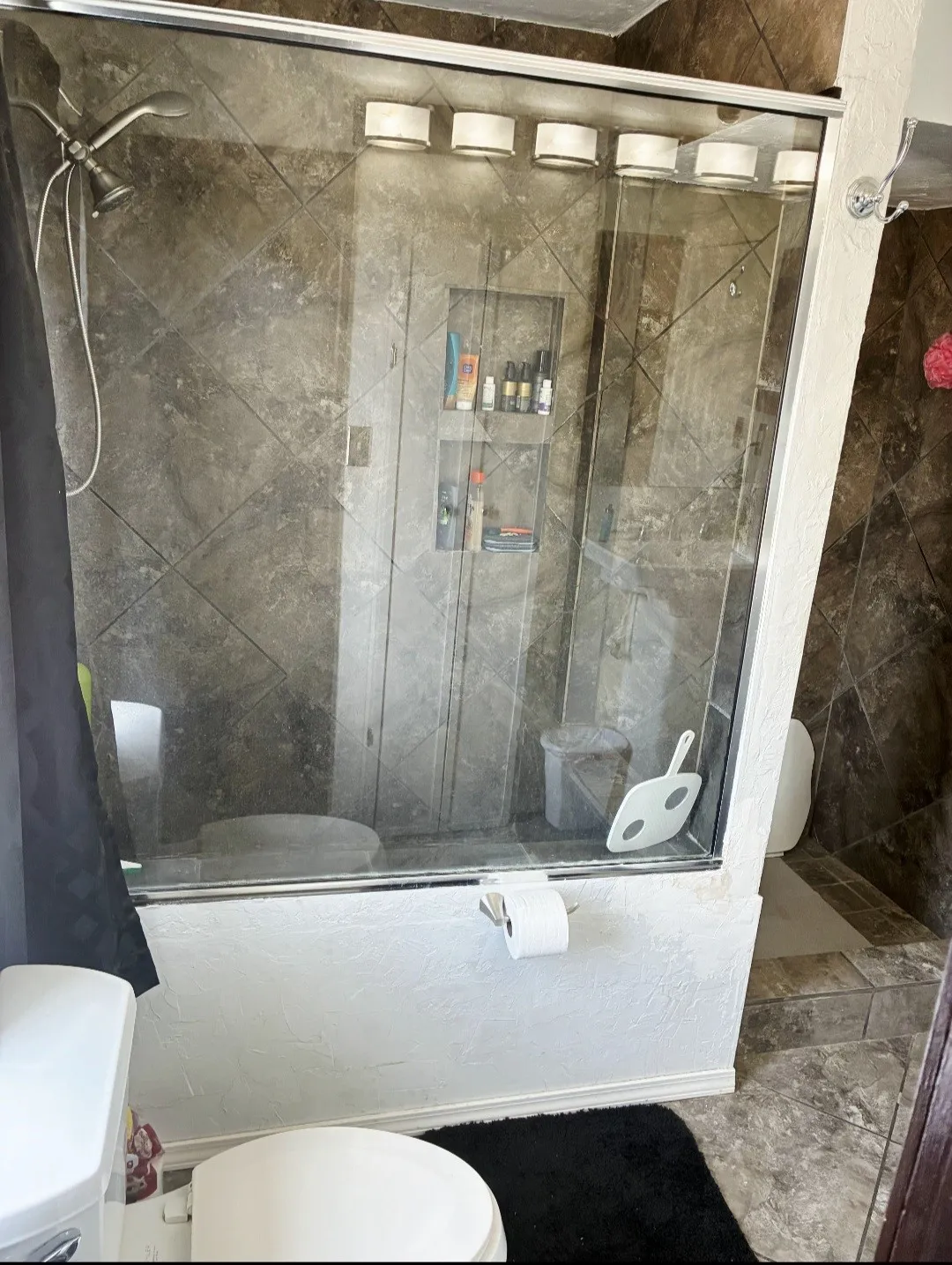 Glass-enclosed shower with tiled walls and built-in shelving