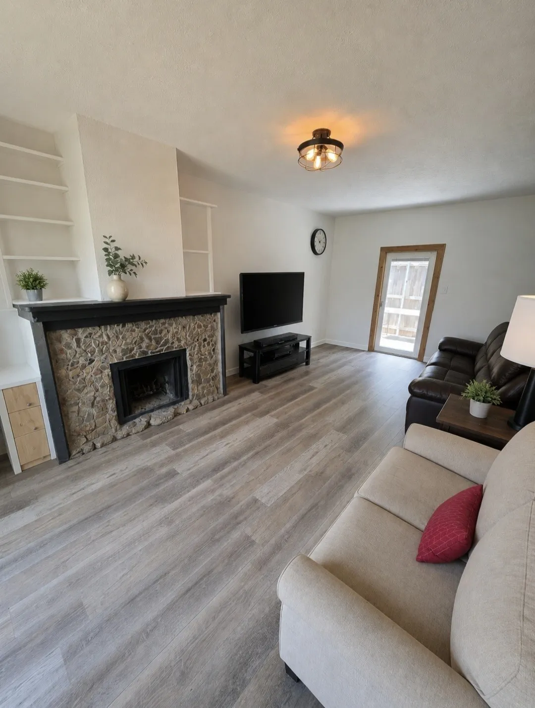 Stone fireplace with a dark wood mantel, wood-finish flooring, built-in shelving, and a glass-paned door