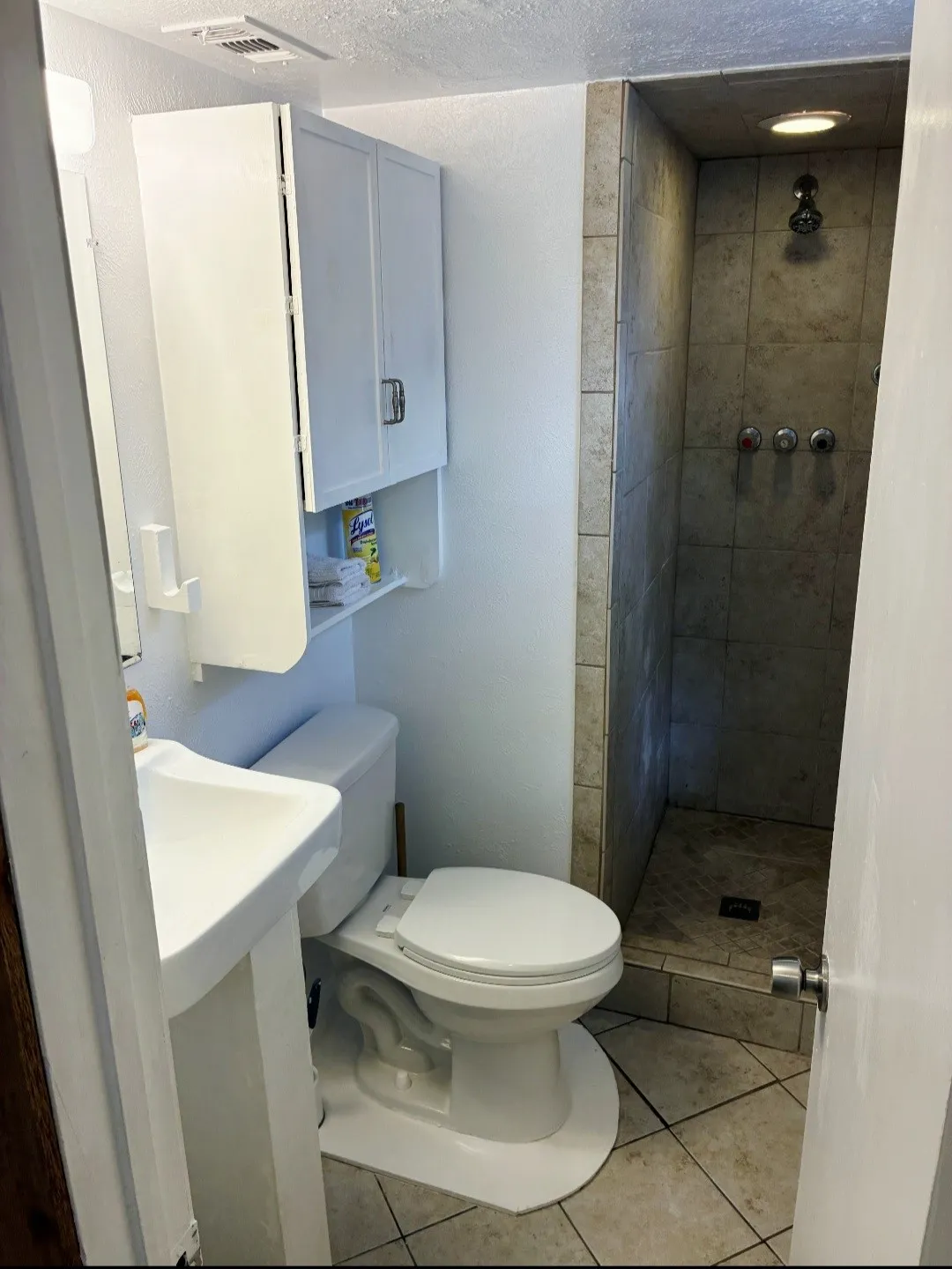 Pedestal sink, wall-mounted storage cabinetry, built-in shower with tile surround, and tiled flooring