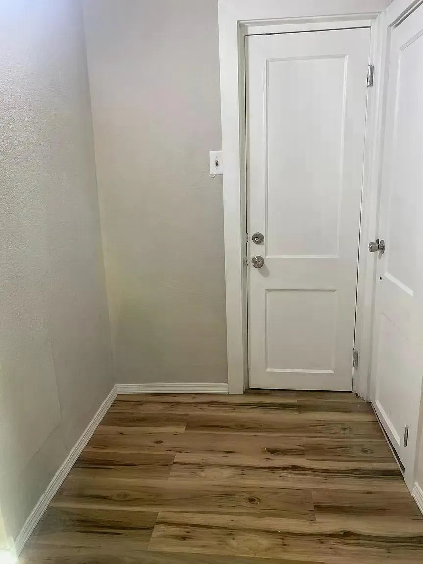 Wood-finish flooring with white trim, two paneled doors, and a wall-mounted light switch
