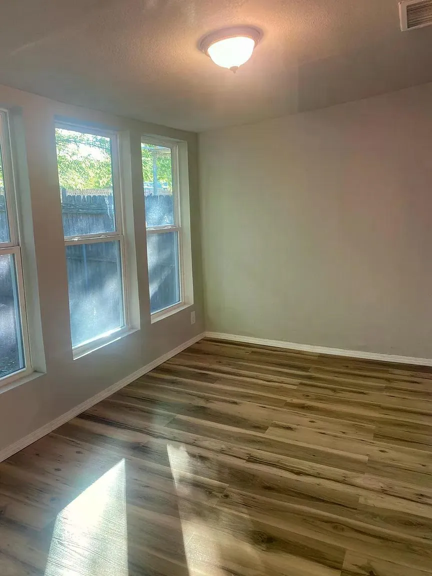 Wood-finish flooring, multiple windows, neutral wall tones, white trim, and a flush mount ceiling light