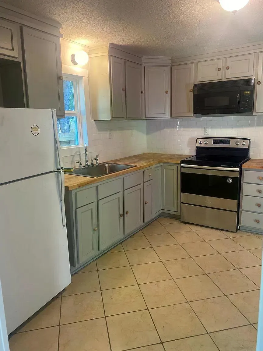 Kitchen featuring light-toned cabinetry, wood-finish countertops, tile flooring, stainless steel range, and a white subway tile backsplash