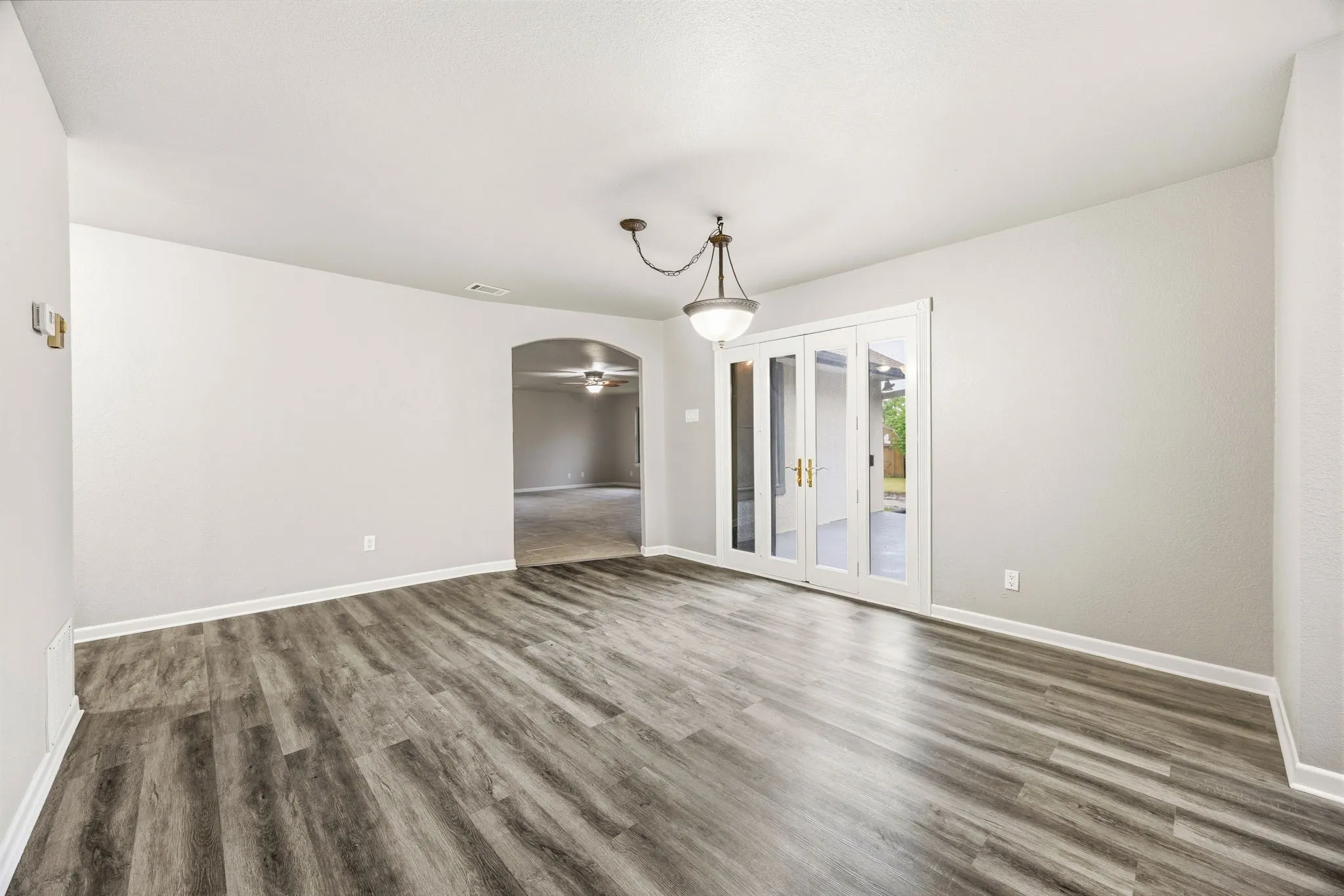 Wood-finish flooring, white walls, built-in ceiling light fixture, arched doorway, and glass-paneled double doors