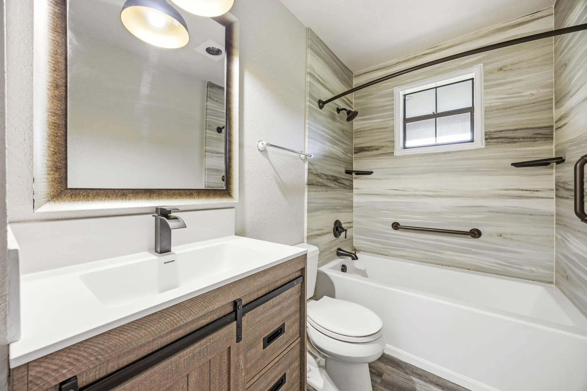 Vanity with integrated rectangular sink and matte black faucet, custom wood-finish vanity with drawer storage, framed mirror, tiled bath enclosure with tub and shower fixtures, and window