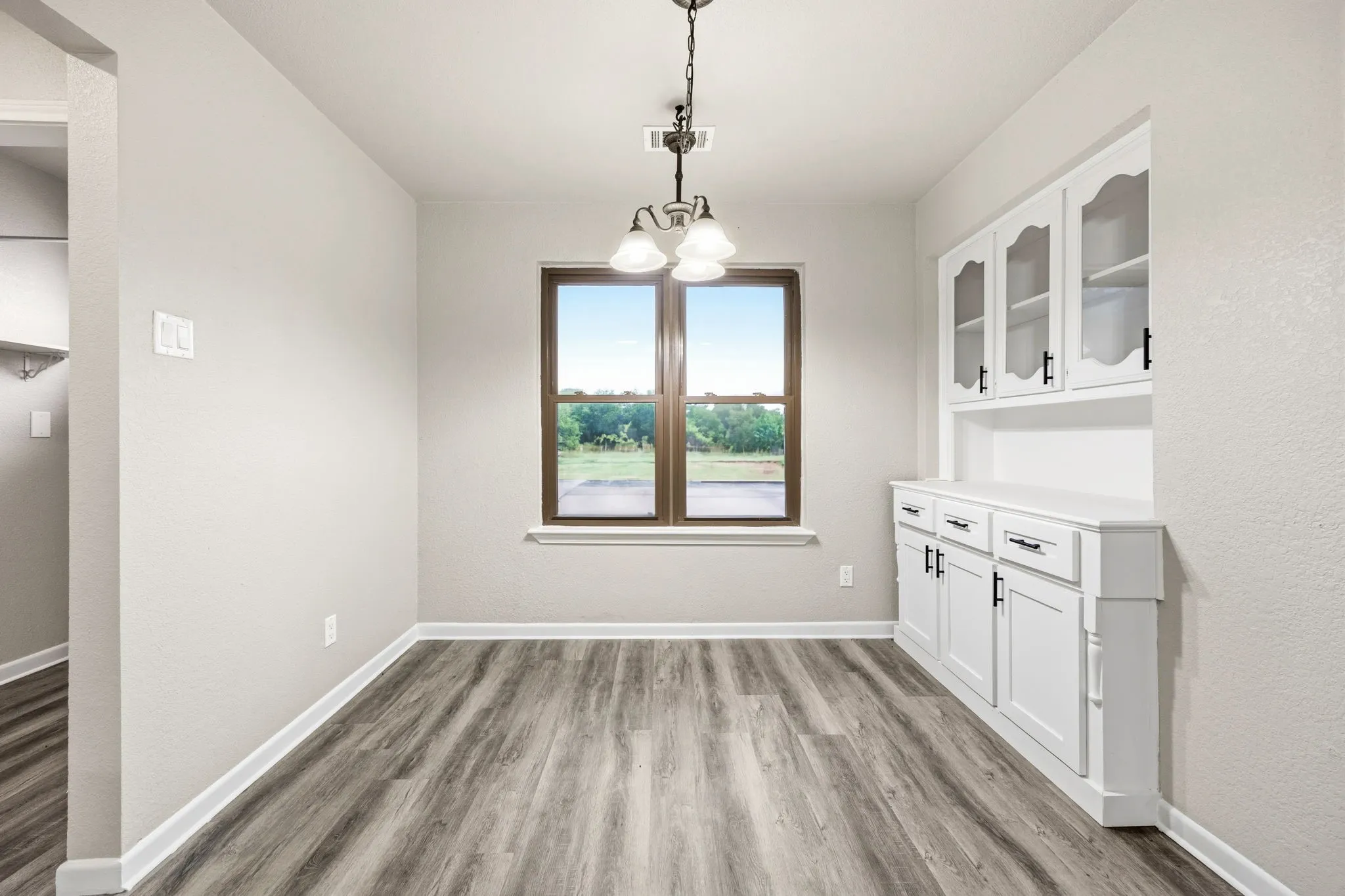 Wood-finish flooring, built-in white cabinetry with glass inserts, recessed lighting, and a single window with dark framing