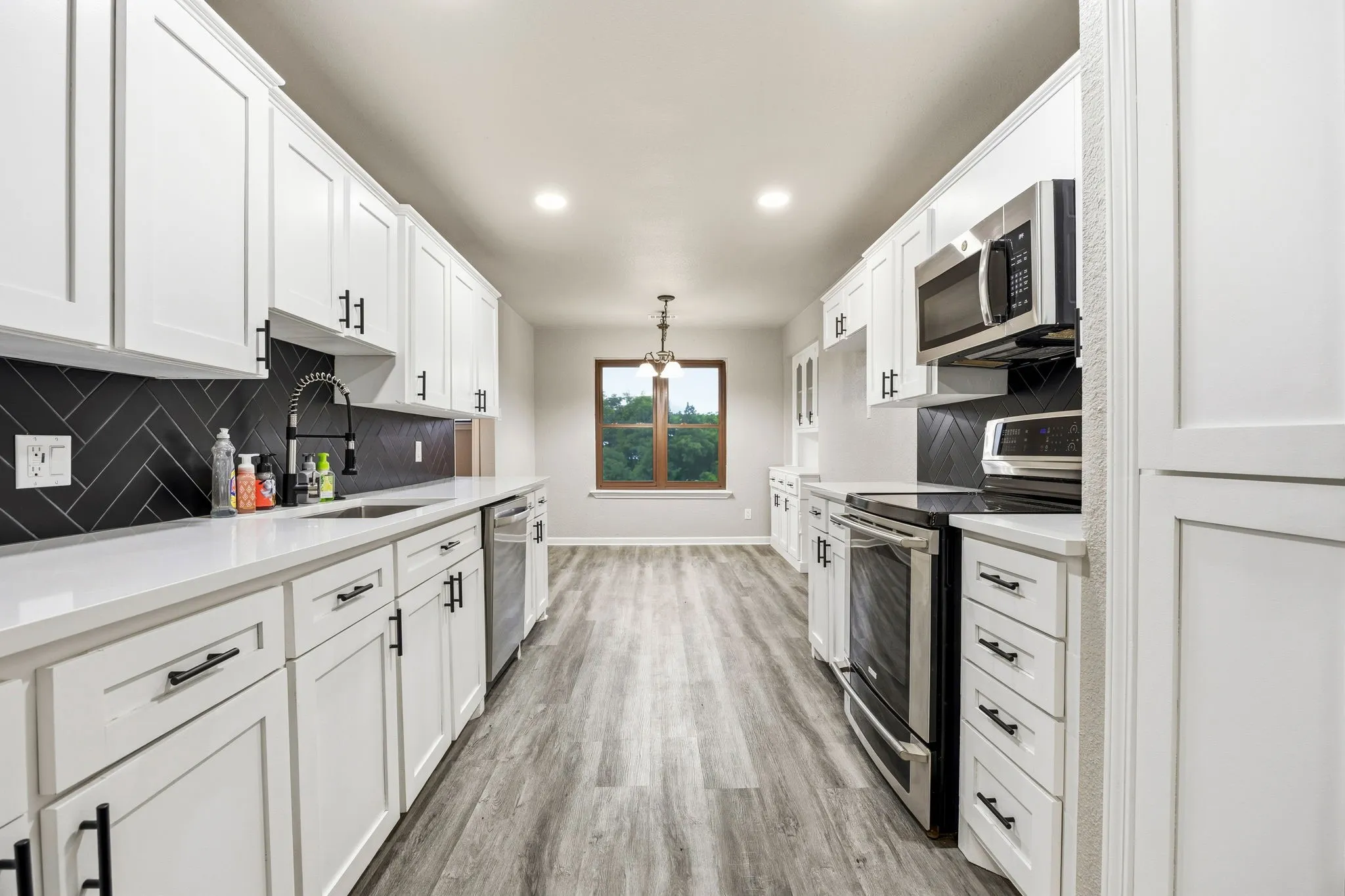 Galley kitchen featuring white cabinetry, stainless steel appliances, herringbone tile backsplash, wood-finish flooring, and recessed lighting