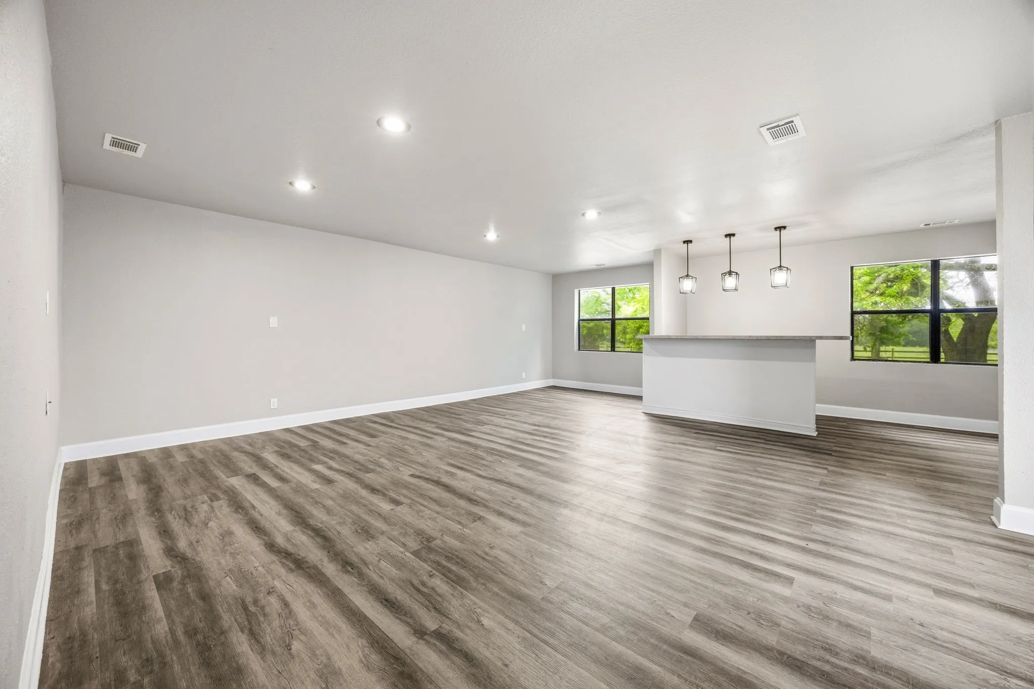 Open-concept living space featuring wood-finish flooring, recessed lighting, and a built-in bar with pendant lighting