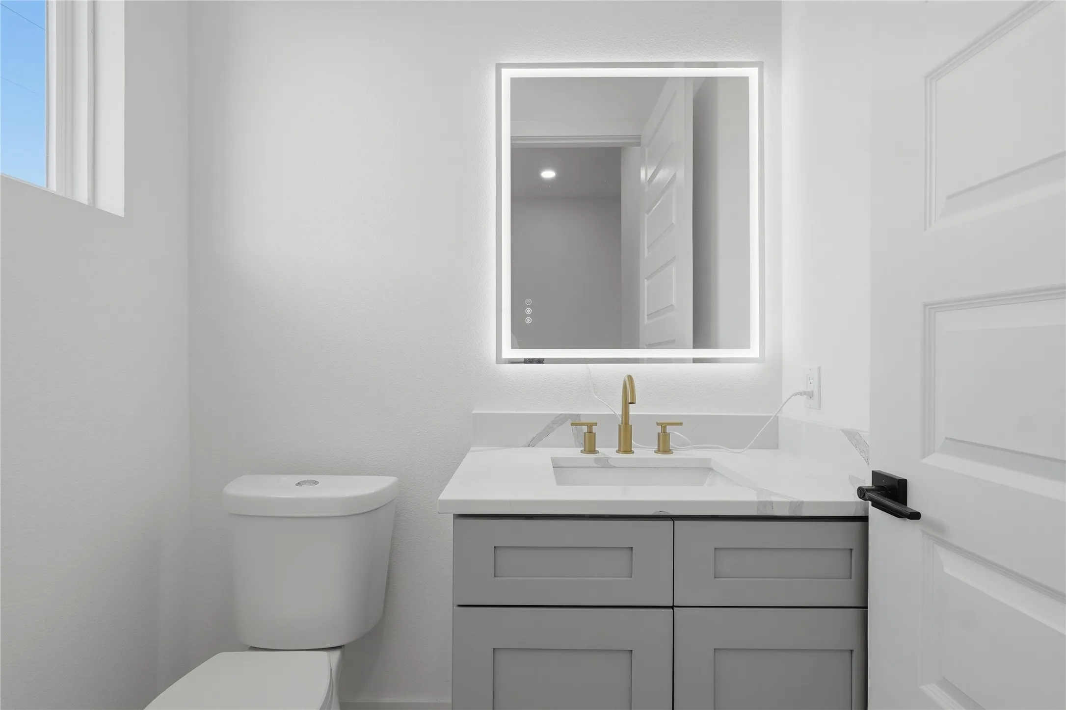 Modern vanity with light gray shaker cabinetry, integrated sink, and gold-finish faucet