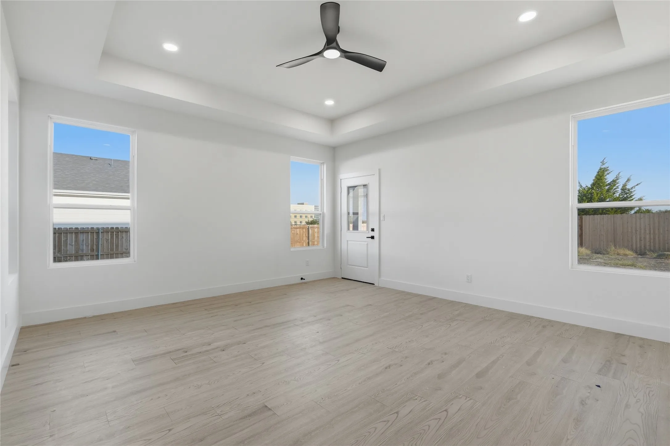 Recessed lighting, contemporary ceiling fan, tray ceiling, wood-finish flooring, and white interior door with frosted glass