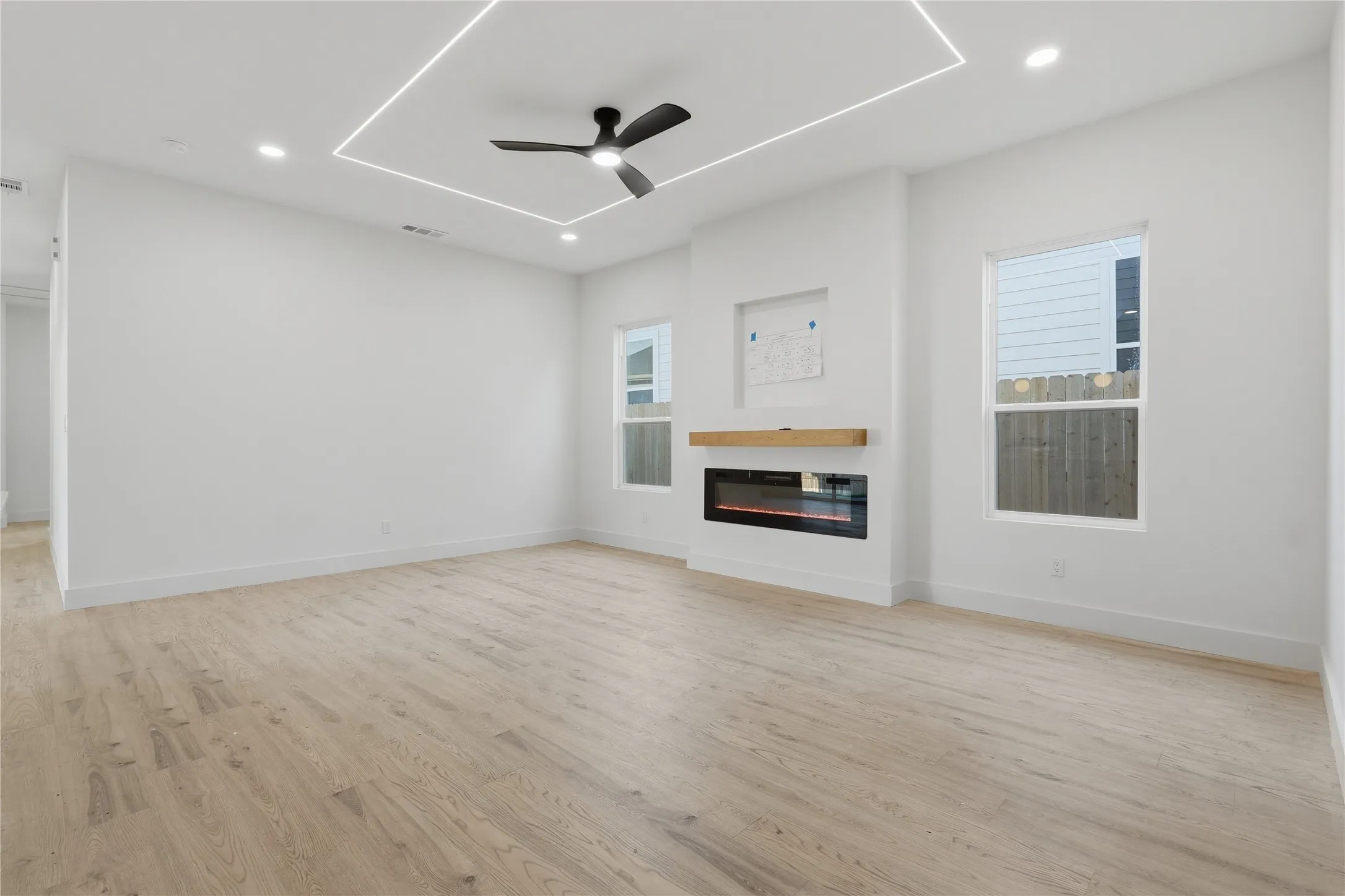 Wood-finish flooring, recessed lighting, ceiling fan, linear LED lighting, and an electric fireplace with a wood mantle