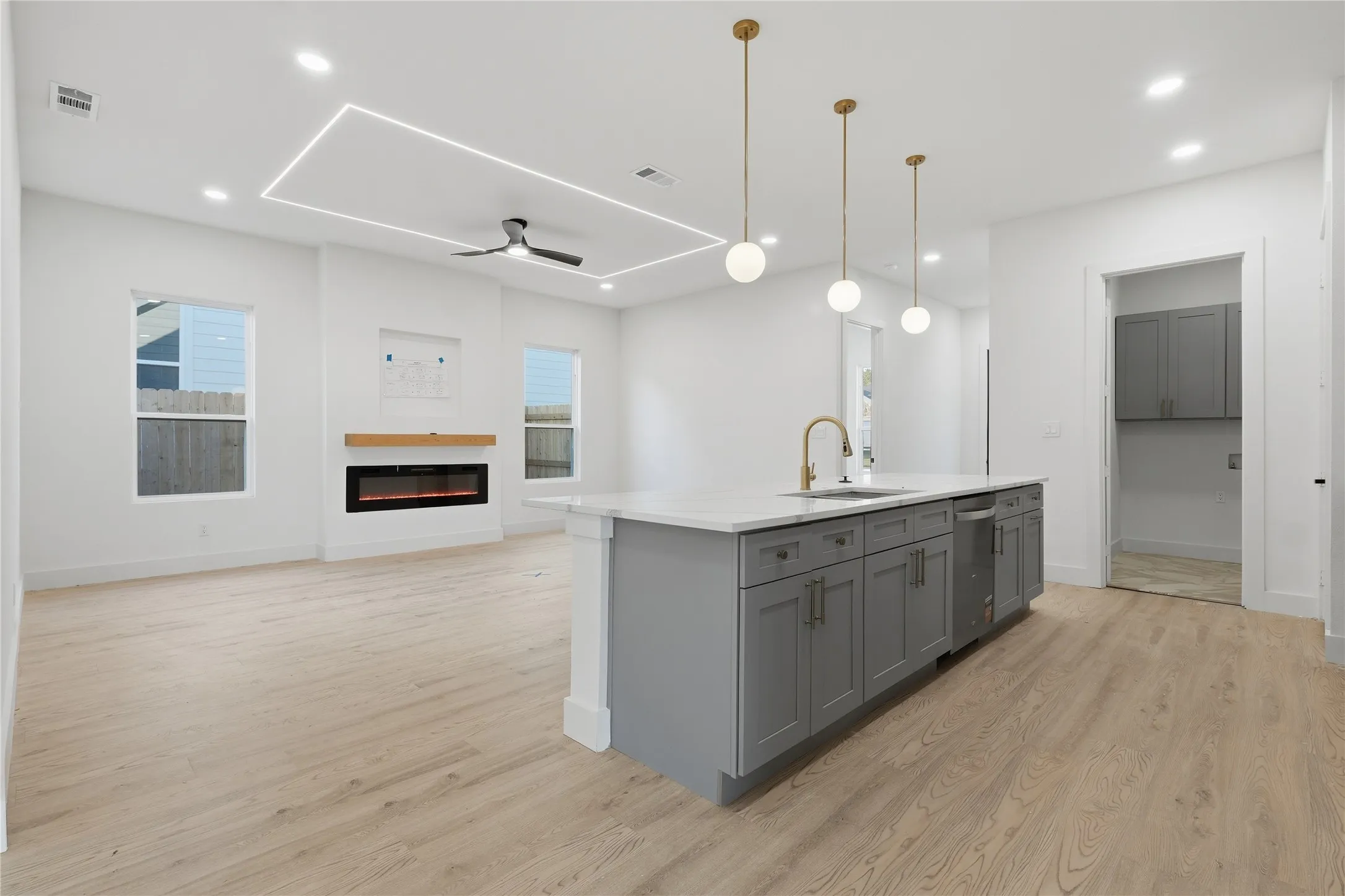 Open-concept living space featuring wood-finish flooring, a modern electric fireplace with a wood mantle, and an island with gray cabinetry and a white countertop