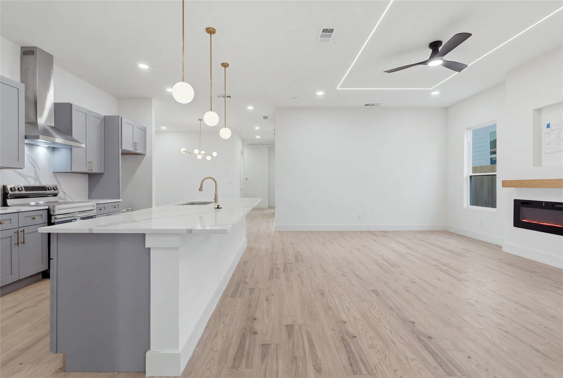 Integrated kitchen and living area featuring wood-finish flooring, a kitchen island with stone countertops, a modern fireplace with a wood mantle, and recessed ceiling lighting
