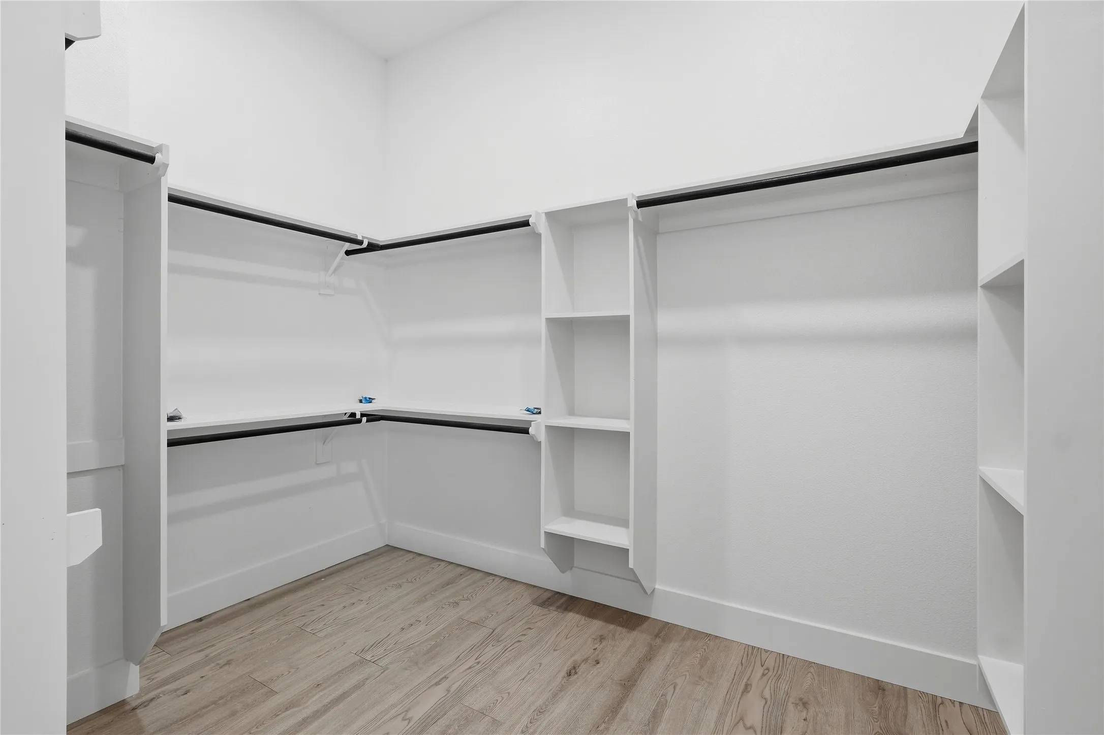 Spacious walk-in closet featuring extensive built-in shelving and hanging rods along multiple walls, wood-finish flooring, and bright overhead lighting for optimal visibility and organization