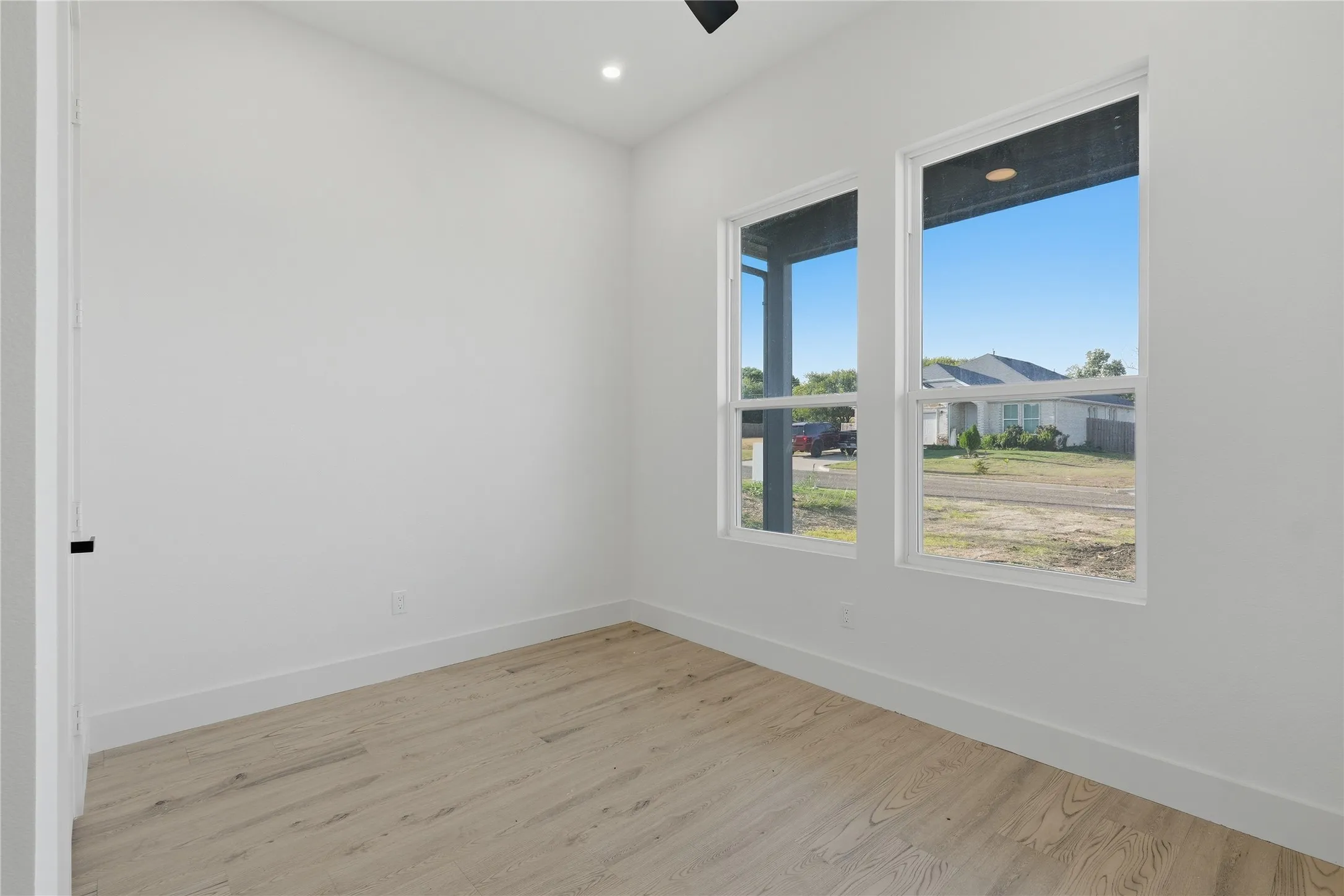 Recessed ceiling lighting, wood-finish flooring, white walls, two double-hung windows, and a black ceiling fan