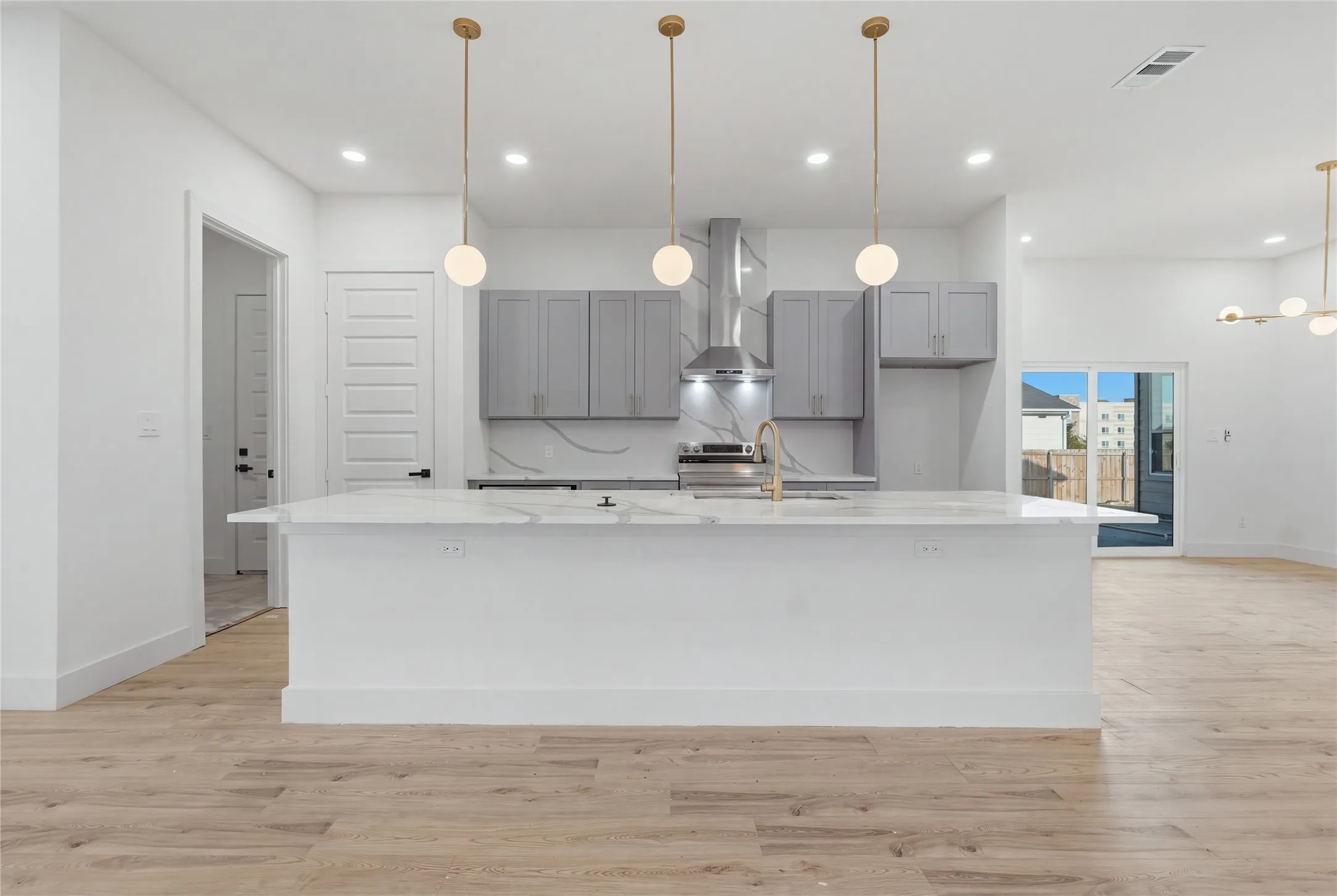 Open-concept kitchen with light wood-finish flooring, white island featuring a countertop, gray cabinetry, and stainless steel appliances