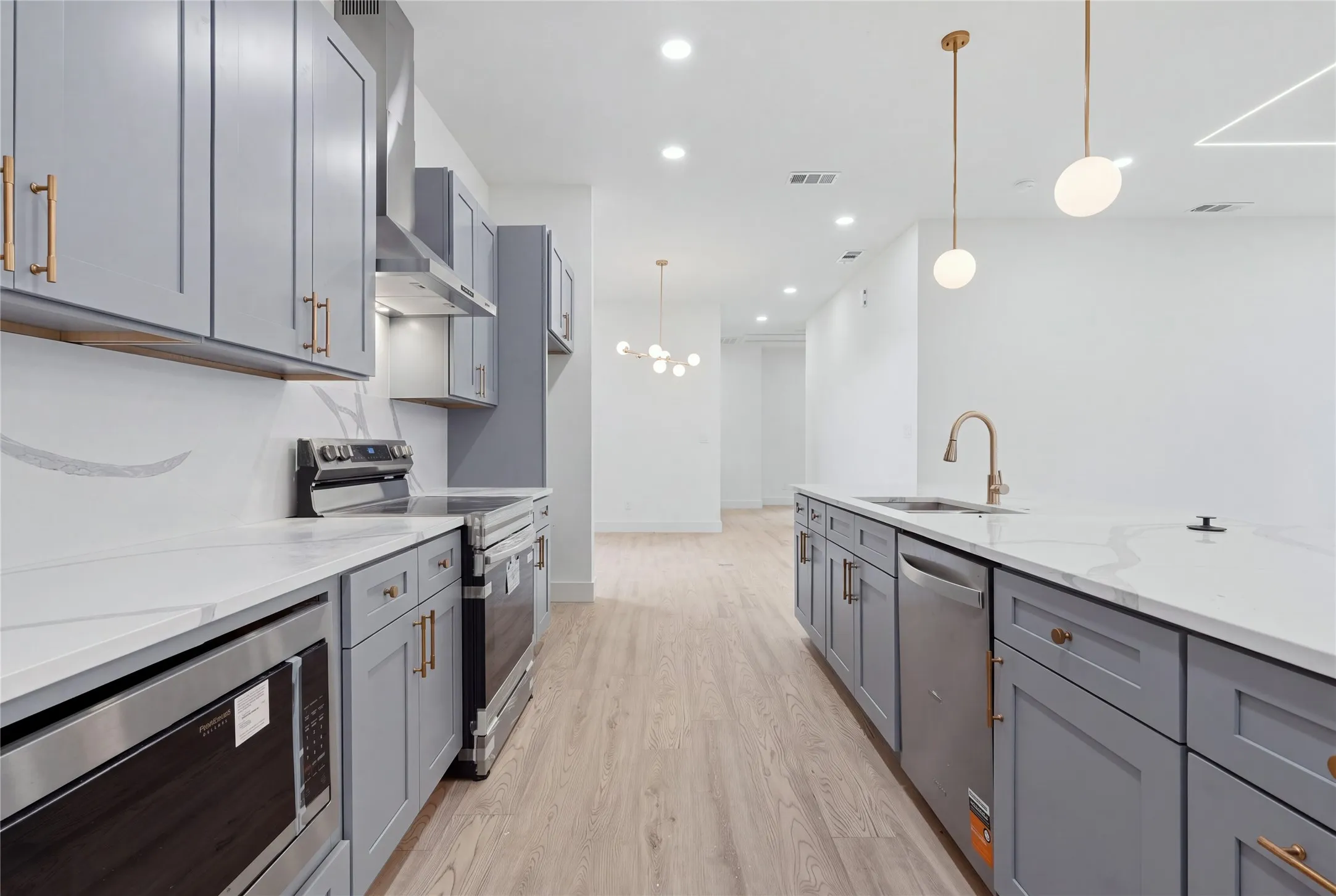 Modern kitchen featuring light gray cabinetry, stainless steel appliances, white countertops, and wood-finish flooring