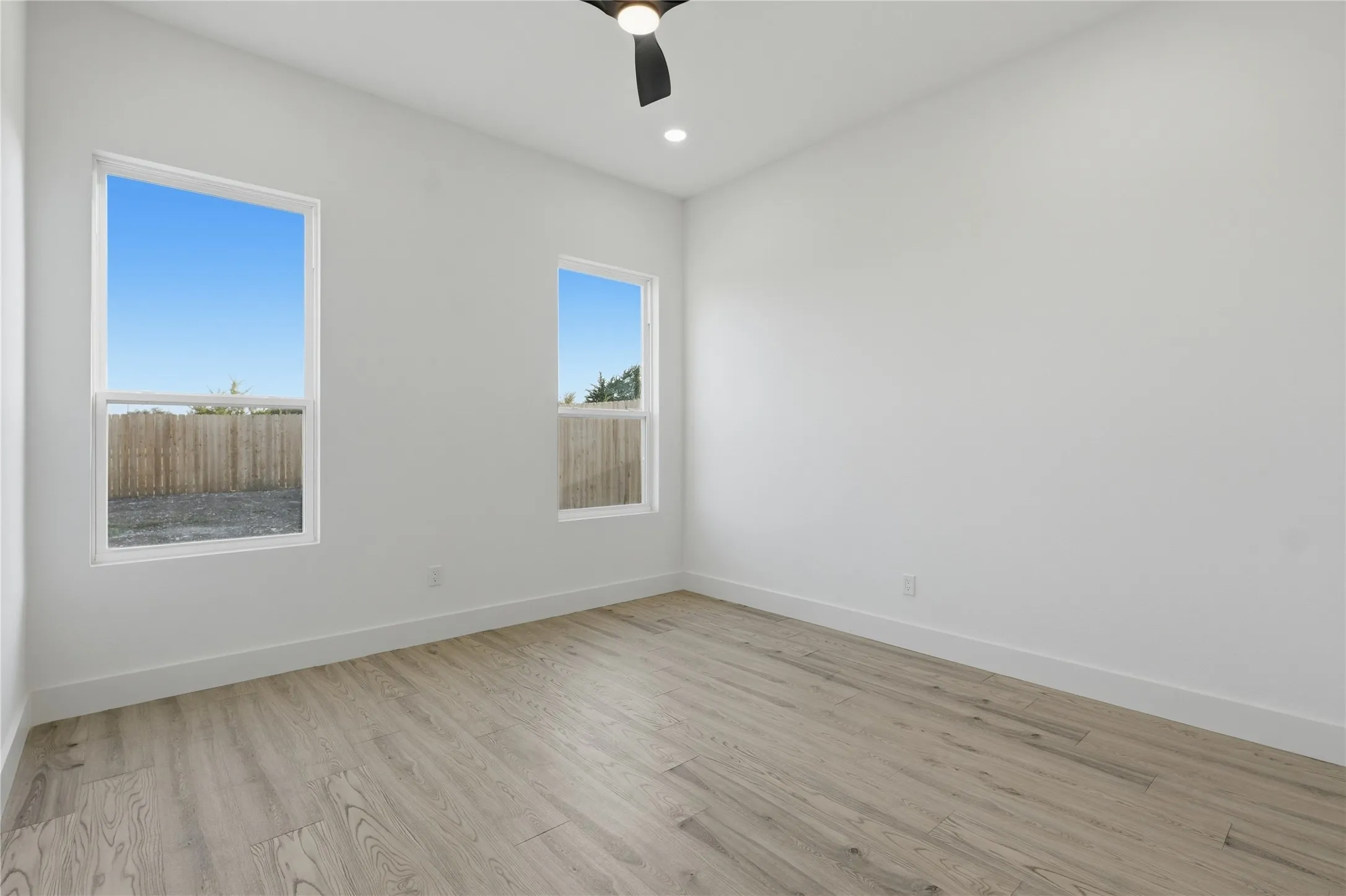 Recessed lighting, wood-finish flooring, two large windows, ceiling fan, and white walls