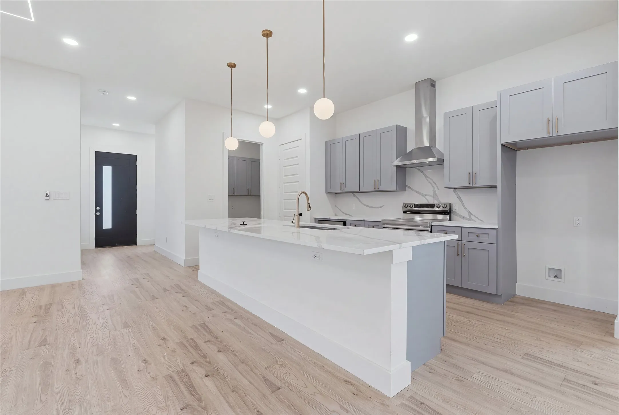 Modern kitchen and open living area featuring white quartz countertops, gray cabinetry with stainless steel appliances, a large waterfall-edge island, wood-finish flooring throughout, and pendant lighting suspended from the ceiling