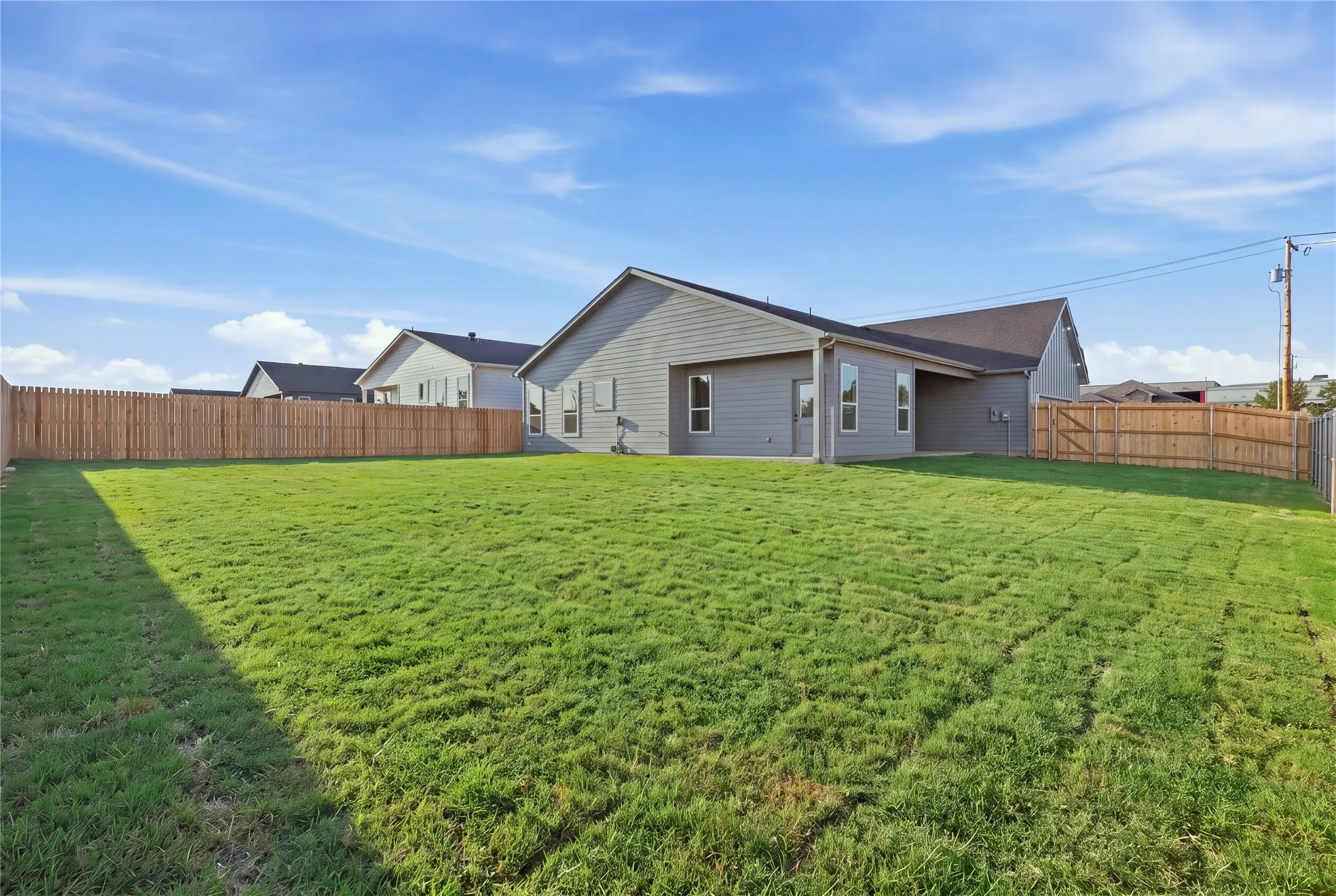 Expansive backyard featuring a manicured lawn, full perimeter wood fencing, and a covered patio area