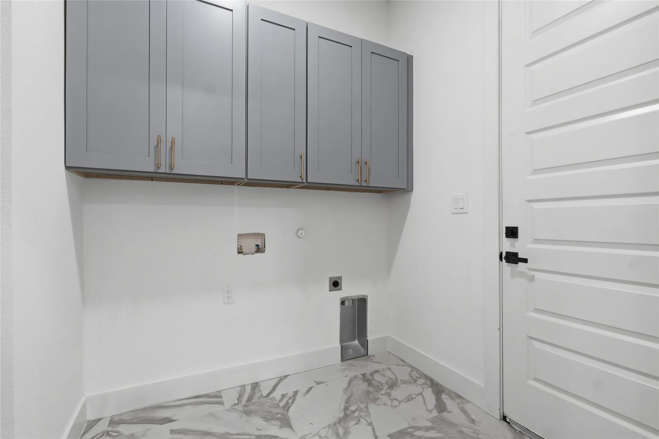 Gray shaker-style cabinetry with gold-tone hardware, white walls, and a white paneled door with black hardware