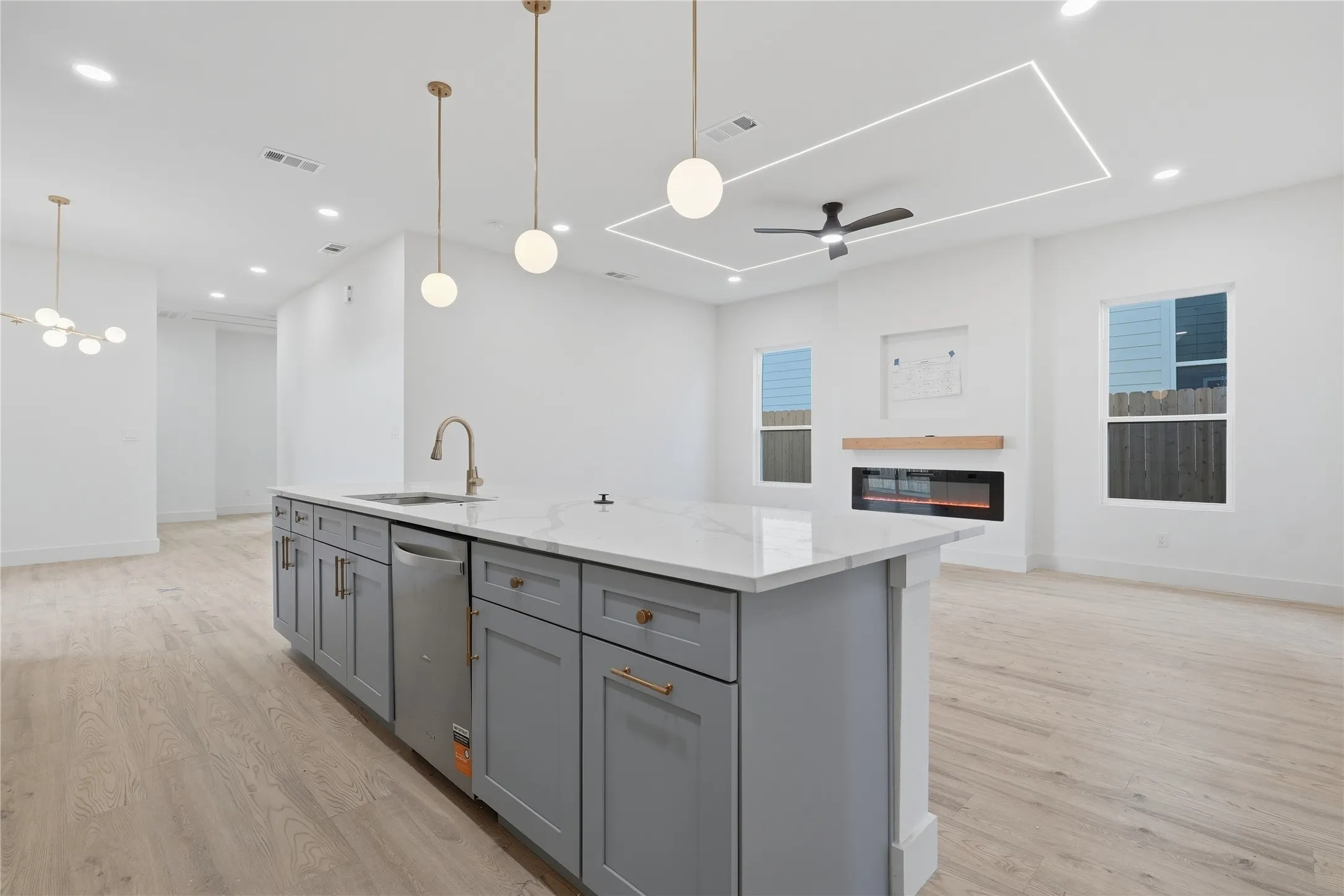 Kitchen island with a light-colored countertop and grey cabinetry, illuminated by three pendant lights