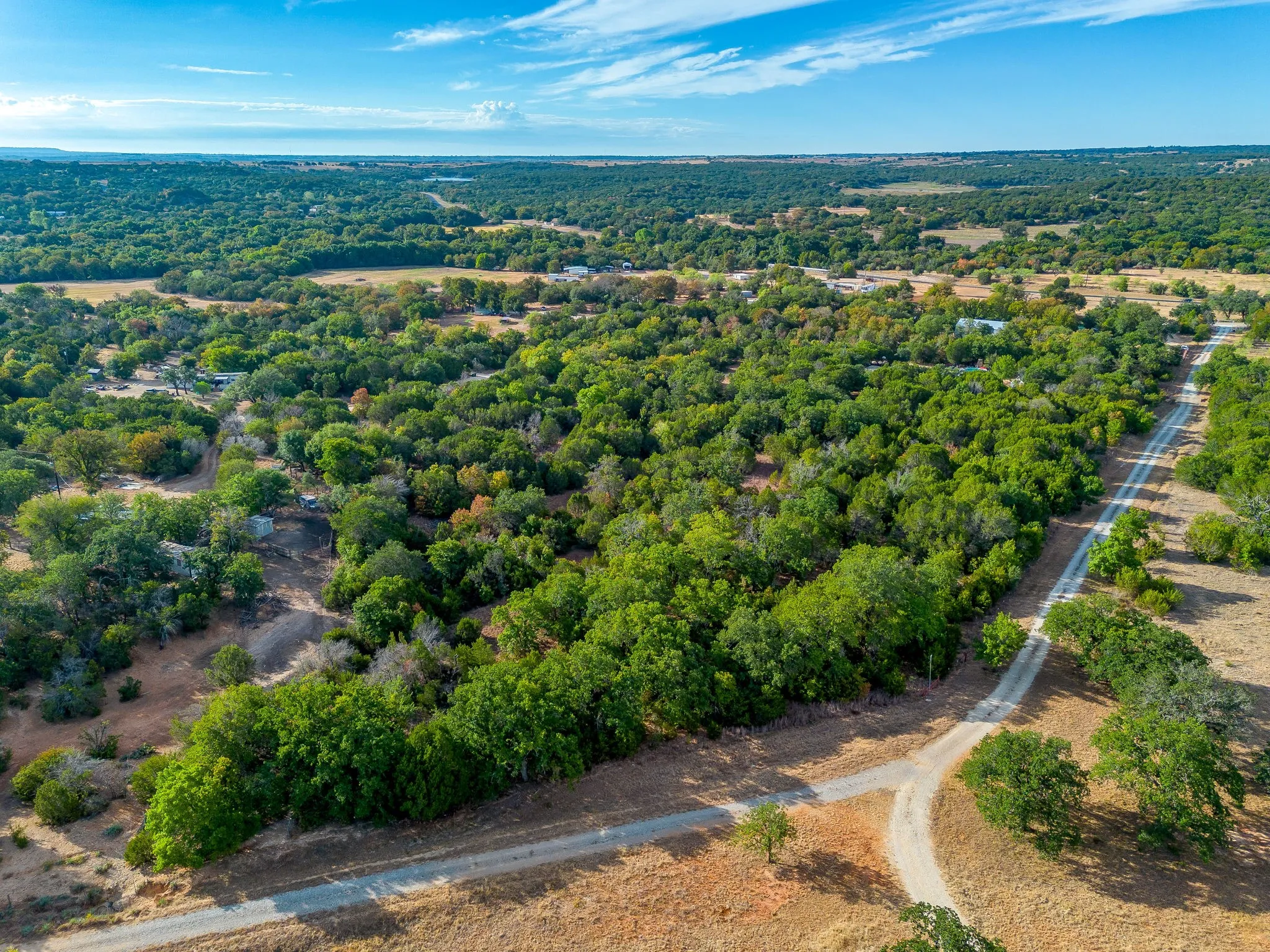 Expansive natural landscape featuring dense tree coverage, open grassy areas, and unpaved access roads