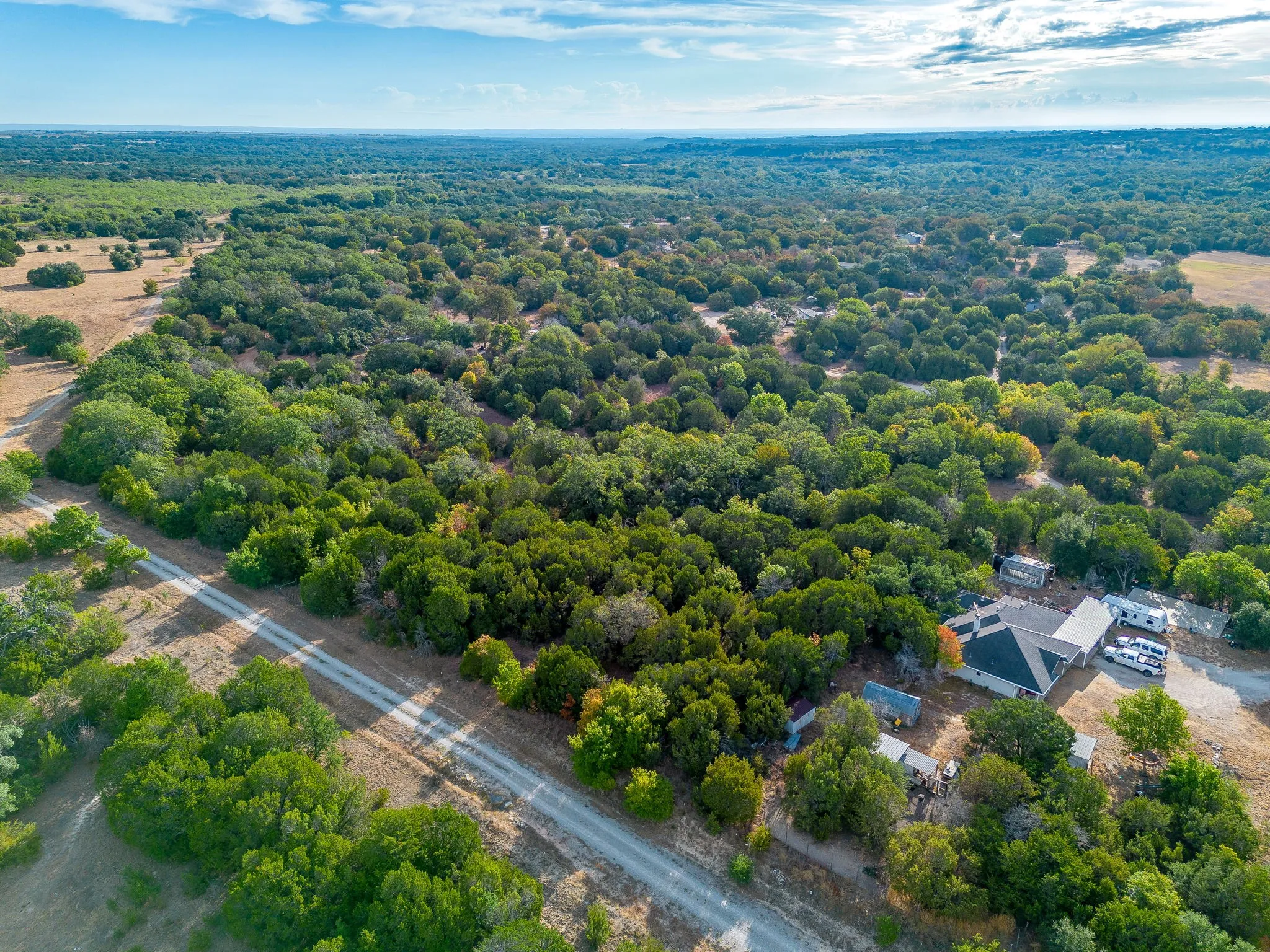 Expansive treed landscape with a gravel driveway and a residential structure featuring a dark roof