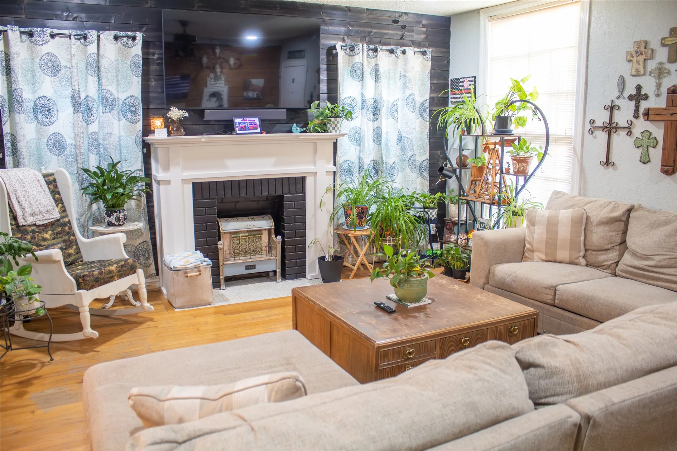 Hardwood flooring, white fireplace mantel, black brick-finish fireplace, and shiplap-style accent wall