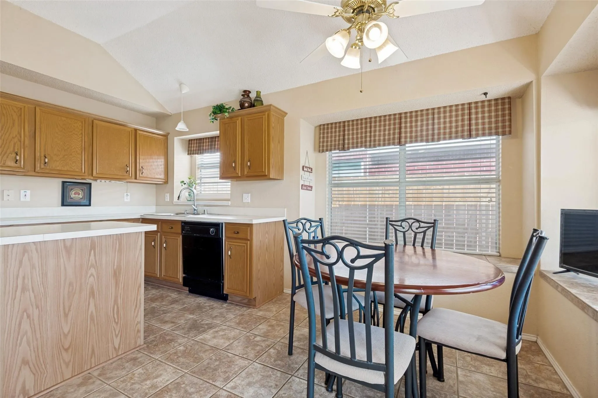 Vaulted ceiling kitchen featuring wood-finish cabinetry, white countertops, a black dishwasher, and tile flooring