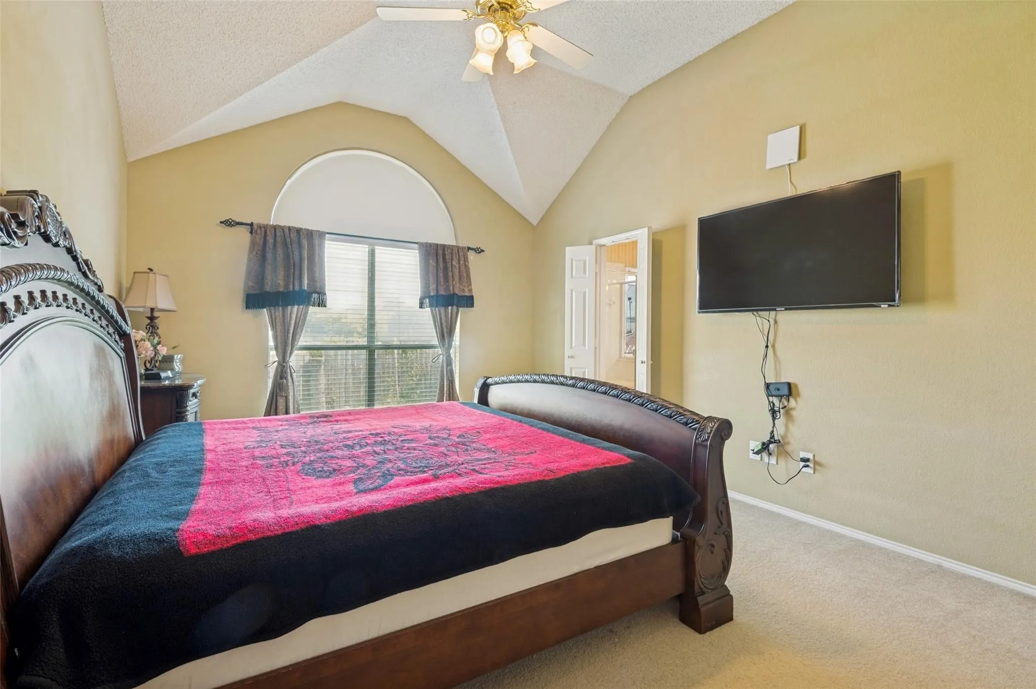 Vaulted ceiling, arched window, ceiling fan, and carpeted flooring