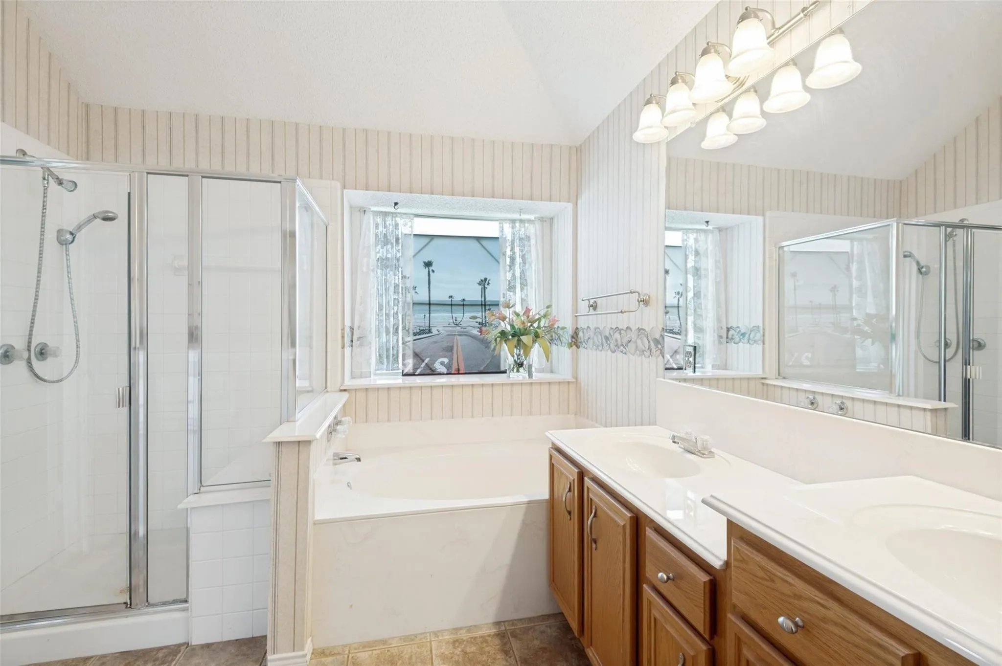 Dual vanity with integrated sinks, built-in bathtub, glass-enclosed shower, and a large mirror