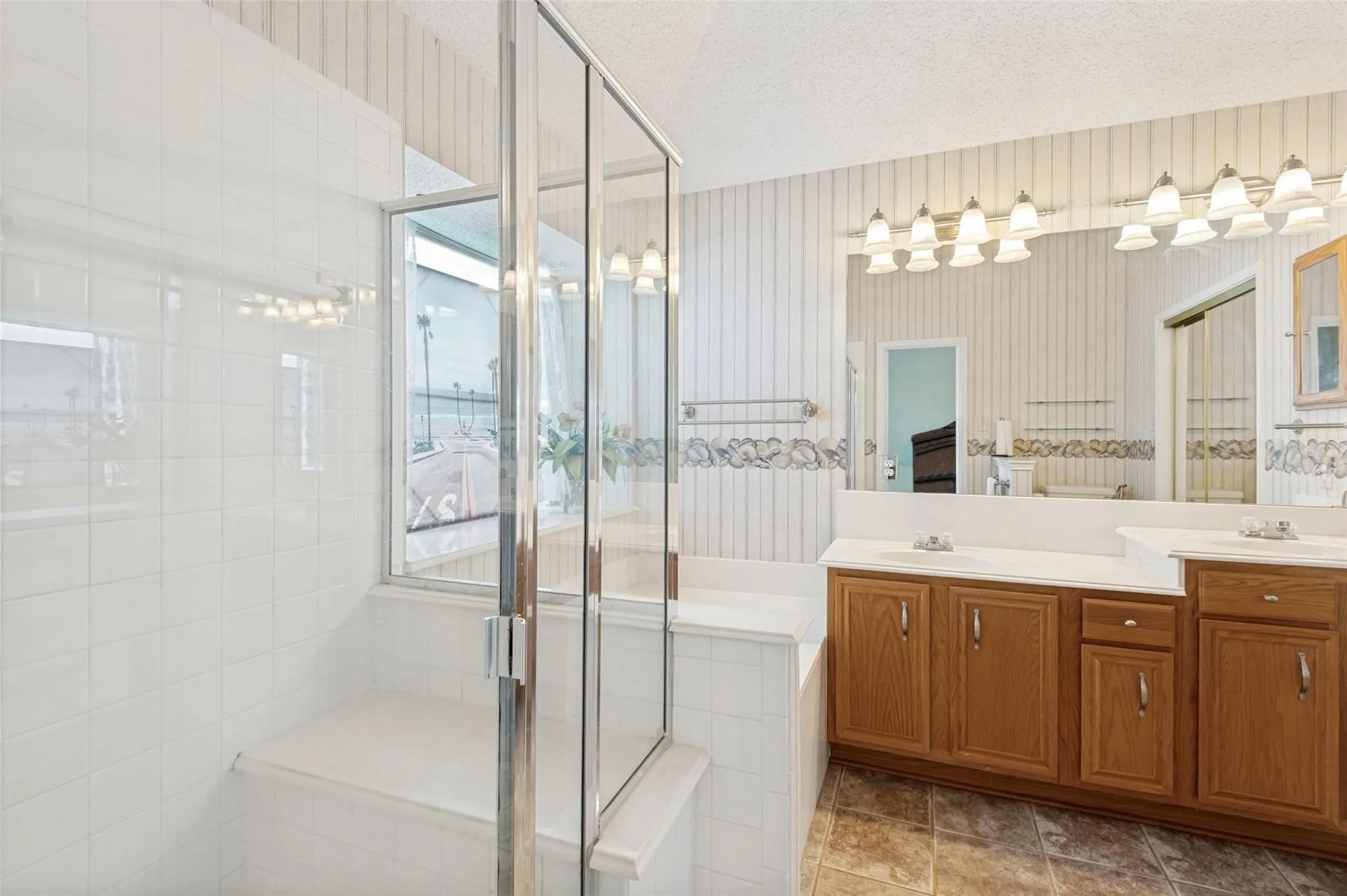 Shower enclosure with clear glass panels, white tile walls, and an integrated bench