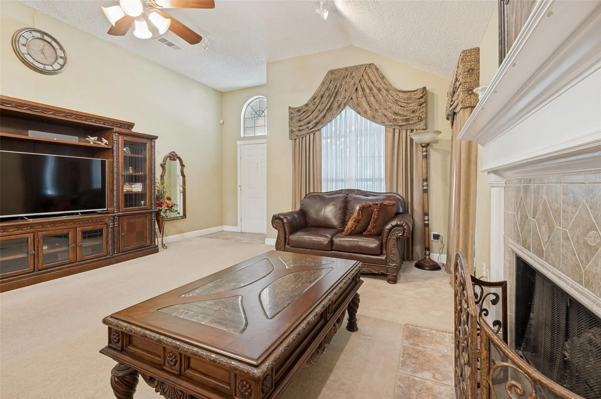Vaulted ceiling, built-in entertainment center, arched transom window, fireplace with tile surround, and decorative mantel