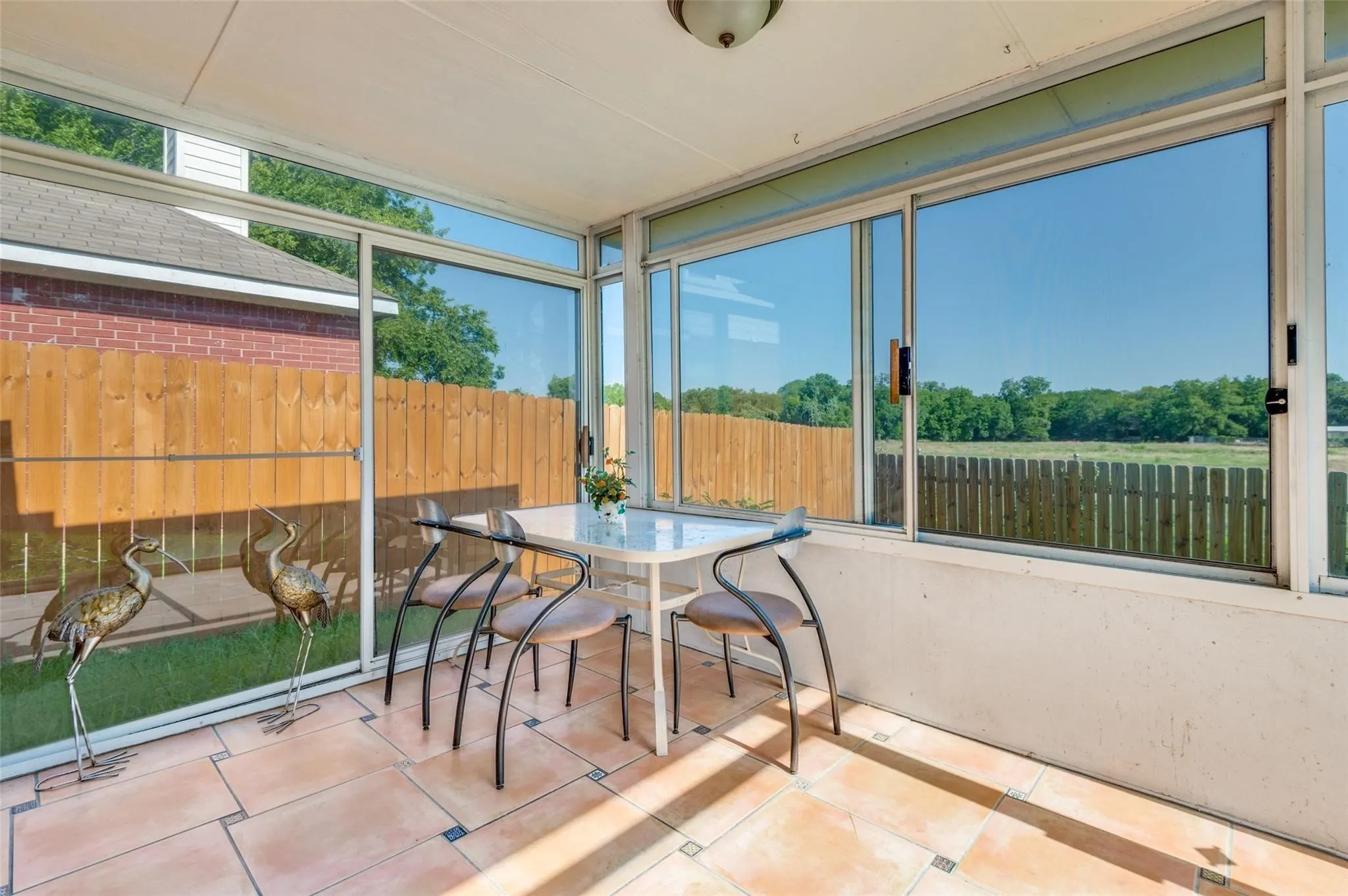 Enclosed patio featuring floor-to-ceiling windows, tile flooring, a slatted wood fence, and a distant field